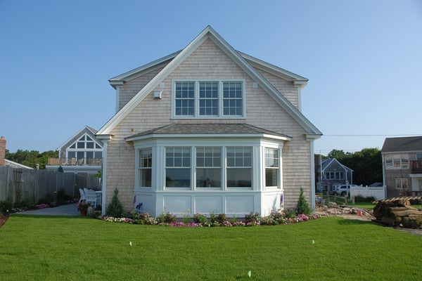 Compact two-story modular home with stone color walls, A-frame design and small grassy lawn