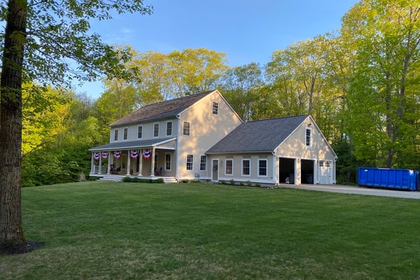 Cape-style modular home with garage attached and large sprawling lawn surrounded by a wood