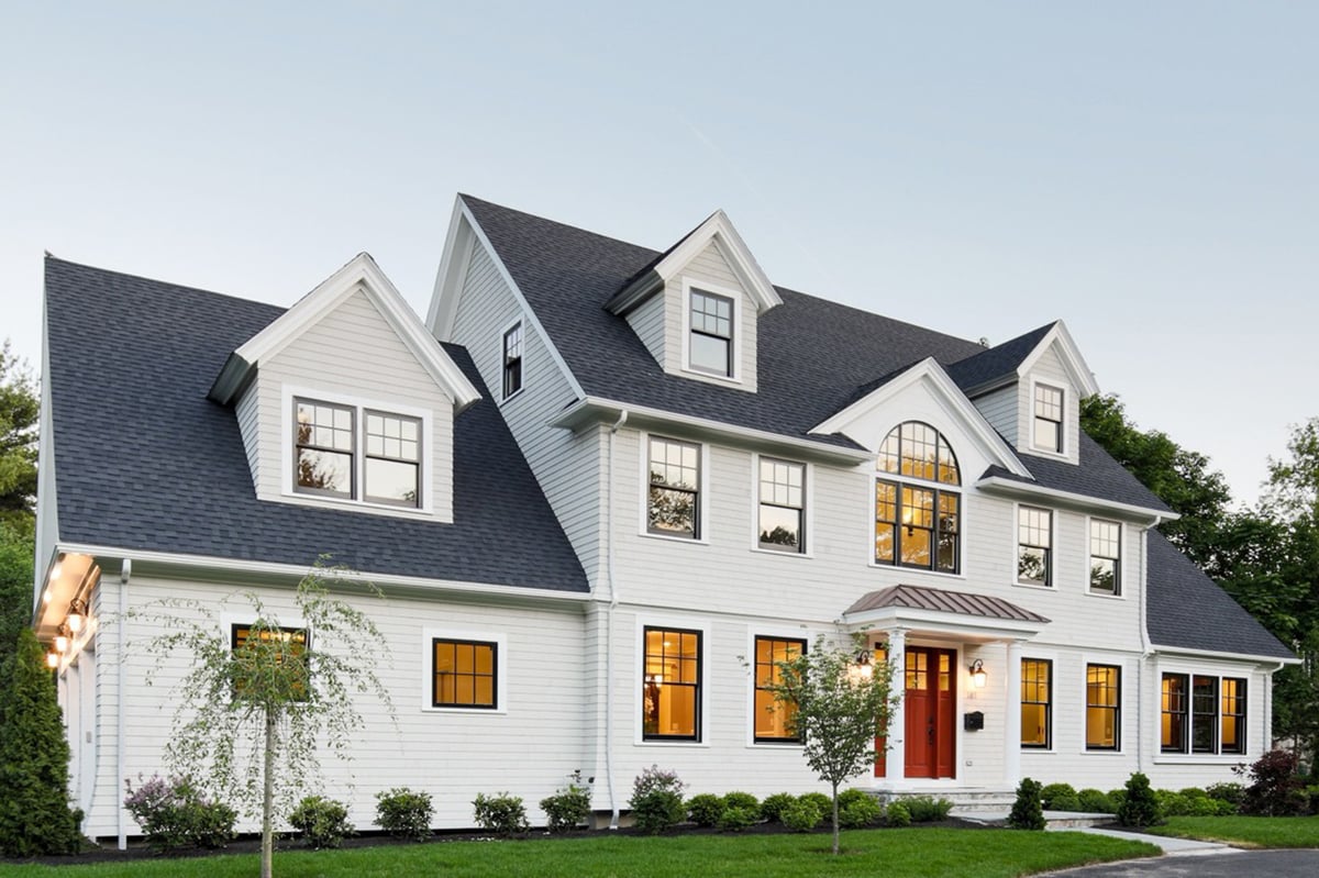 Large two-story modular home with white exterior walls, grey roof, red door, and pristine lawn and garden out front