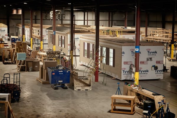 Modular home factory showing a large production line with partially built homes and various pieces of machinery and equipment