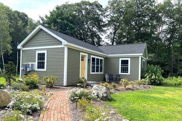 ADU (Accessory Dwelling Unit) with light green walls, grey roof, and yellow door surrounded by a lush yard and small brick path leading to it