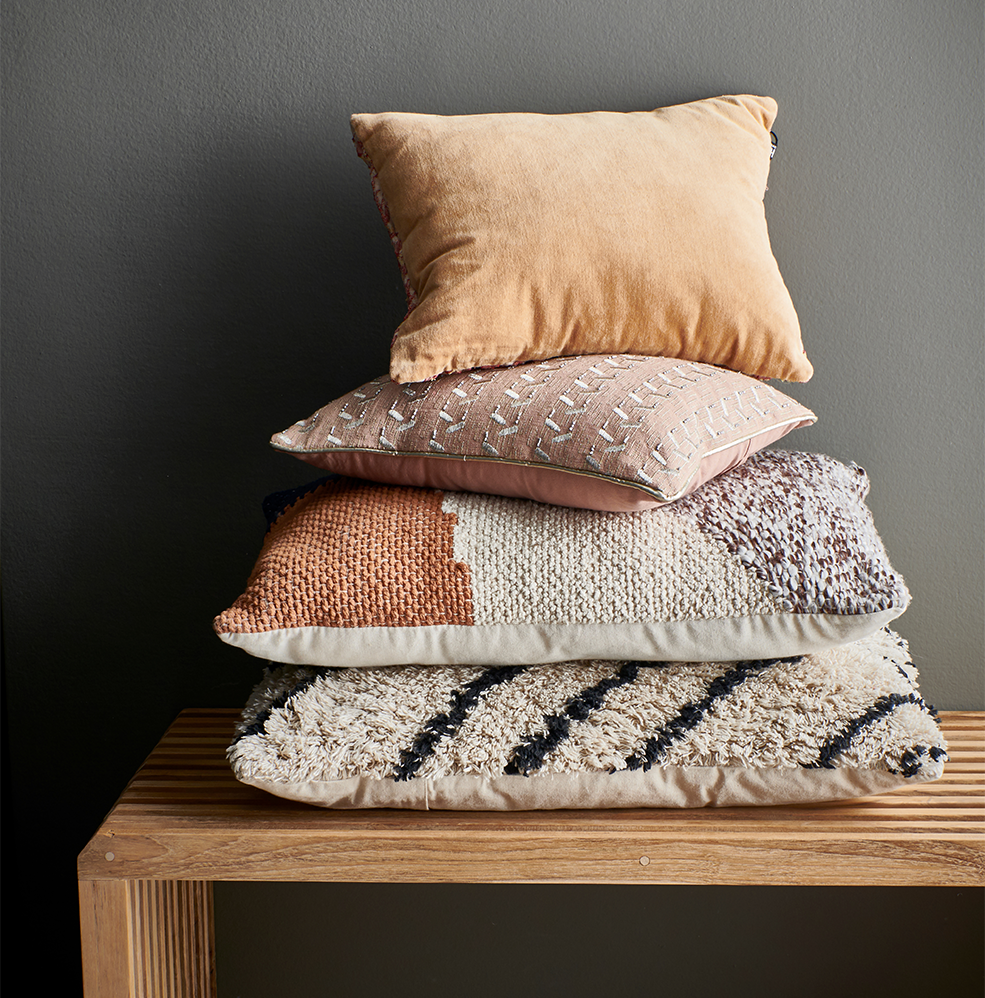 kussen nude met zilveren patches van hkliving op een houten tafel met meerdere kussens en een zwarte muur