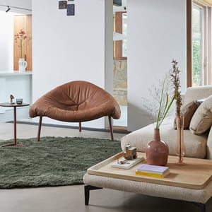 fauteuil tripoli van label van den berg leder bruin met accessoires een groene vloerkleed en witte muren