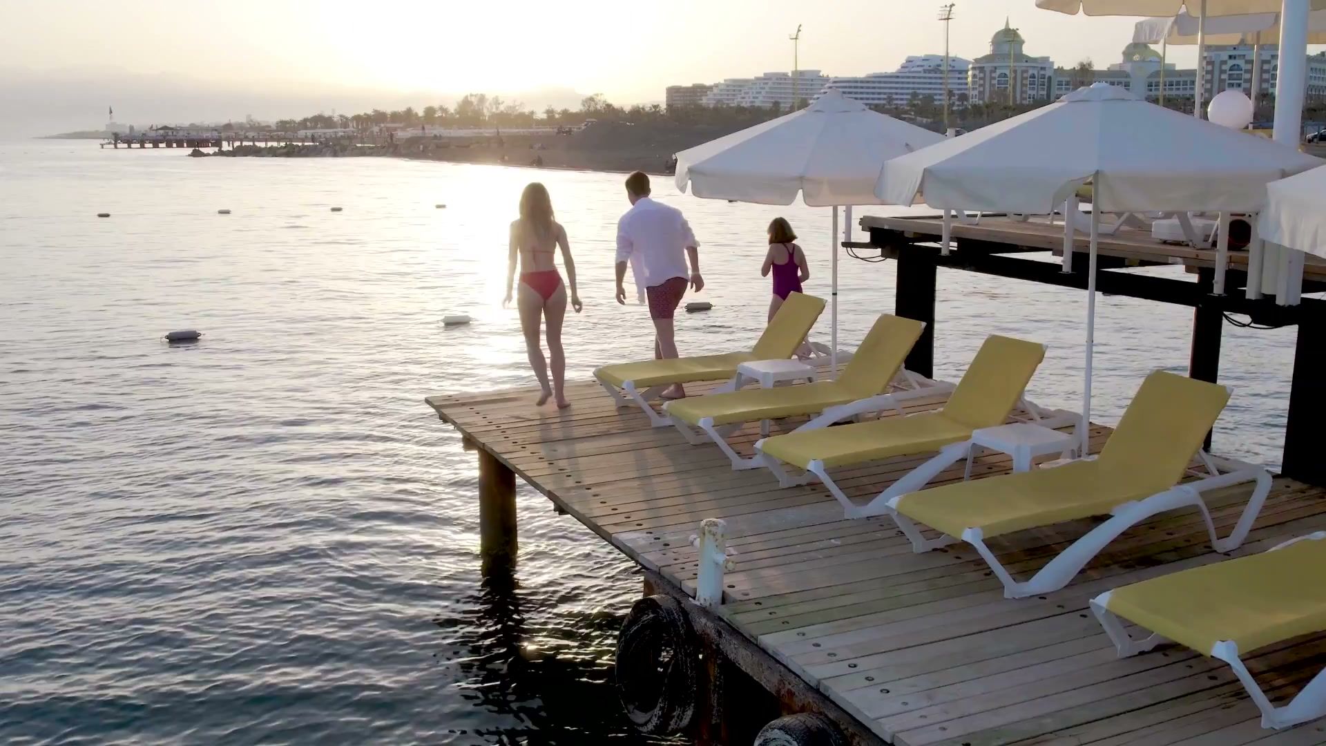 A family heading into the sea from the pier at sunset