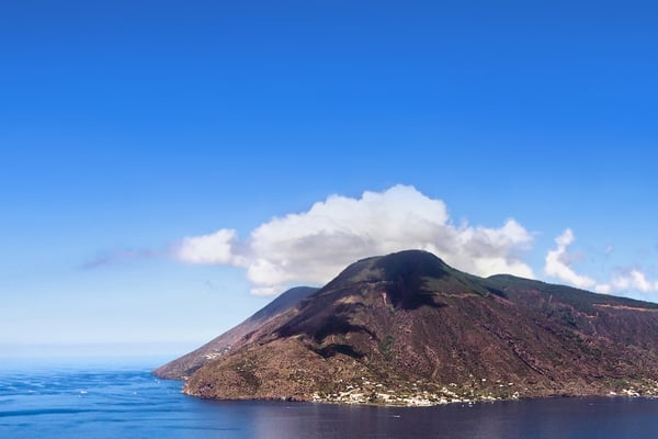 La isla de Stromboli vista desde el agua, su pico volcánico sobresaliendo sobre el tranquilo mar azul.