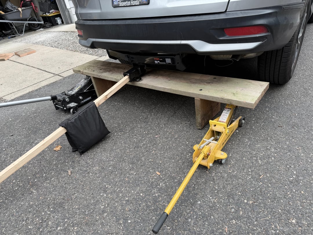 Two floor jacks supporting a plank under a Honda CR-V holding a CURT trailer hitch in position