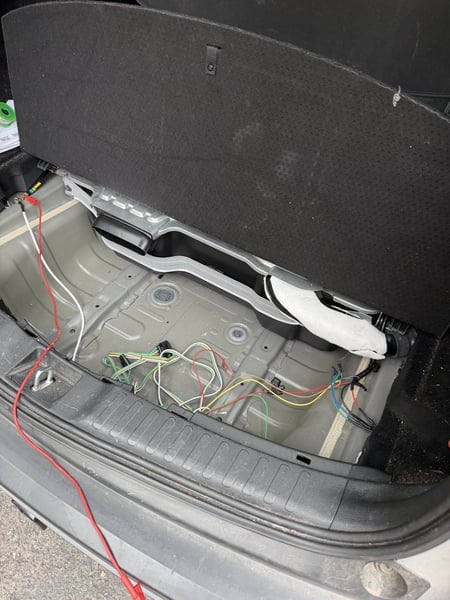 Trailer converter module wiring routed across the trunk pan of a Honda CR-V with the plastic cargo tray removed