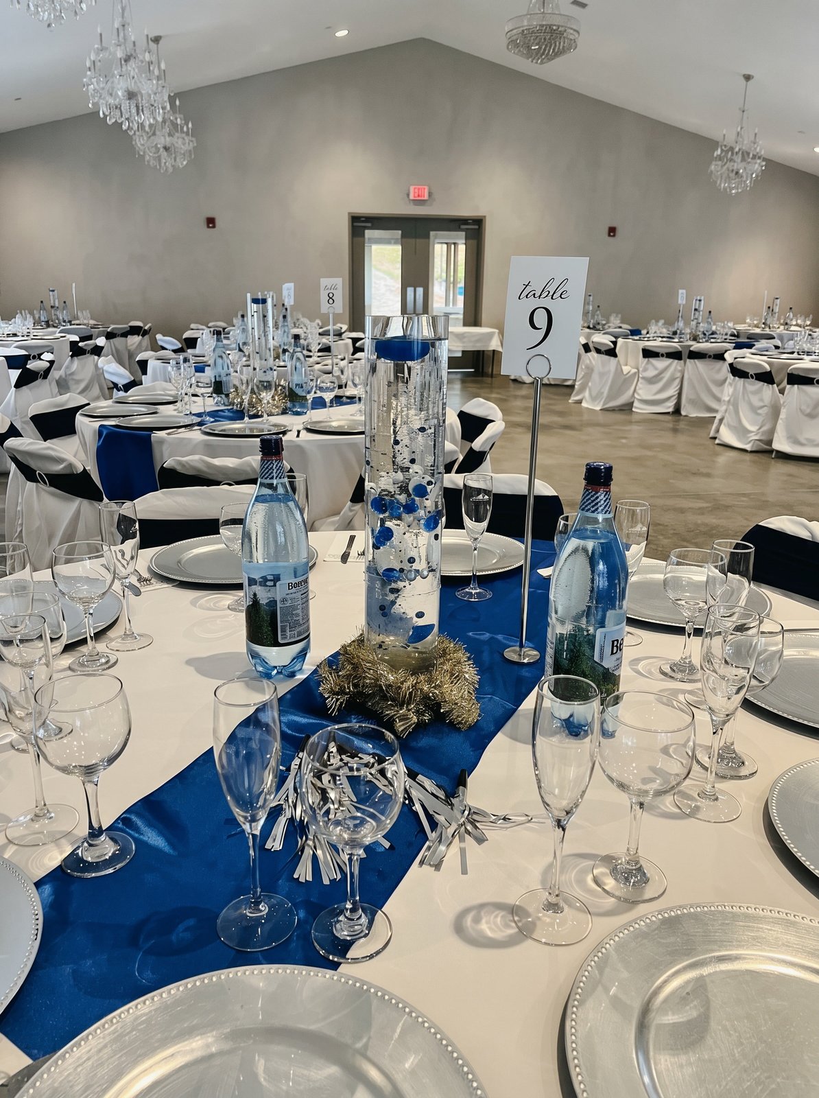 Close-up place setting with a navy blue runner, silver charger plates and a table number card