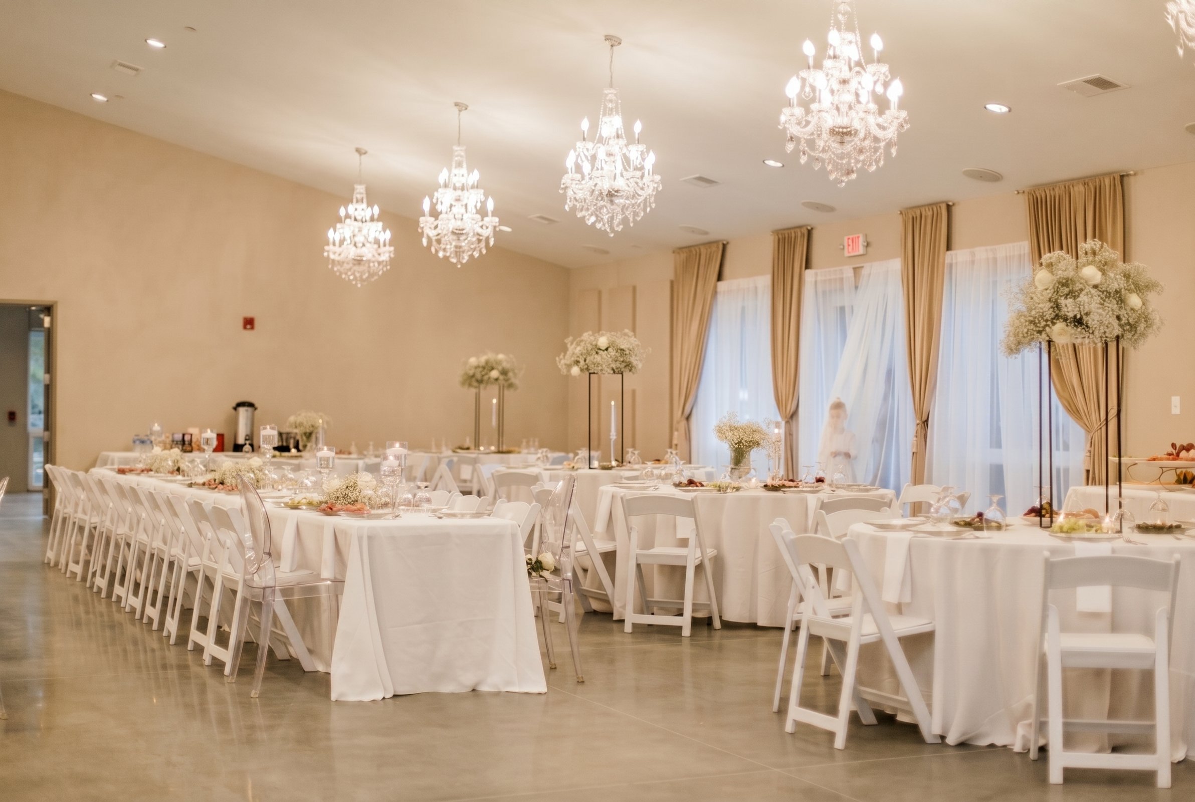 Long banquet tables in white linens with tall floral centerpieces under crystal chandeliers at Fellowship Event Hall