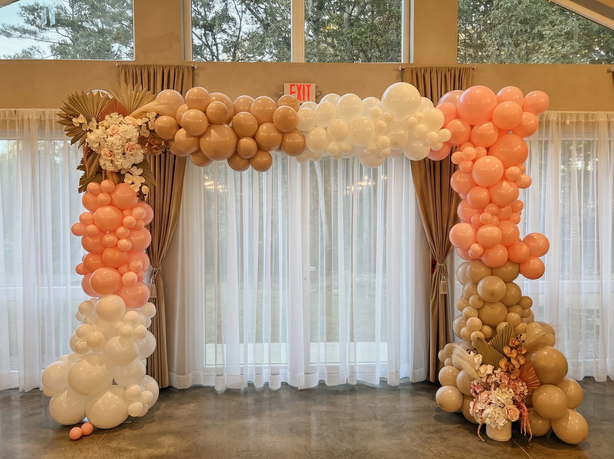 Peach and terracotta balloon arch with dried florals framing the sheer-curtained window wall