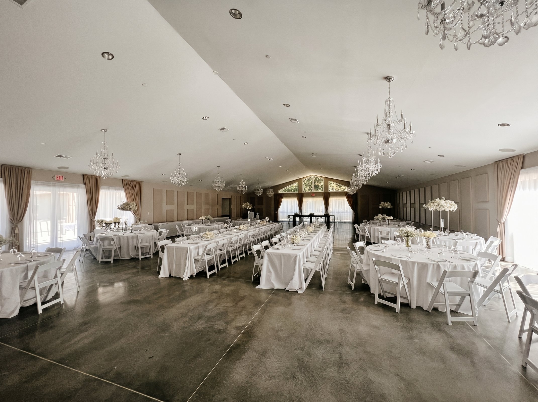 Banquet tables and white folding chairs arranged around an open dance floor in the vaulted main hall