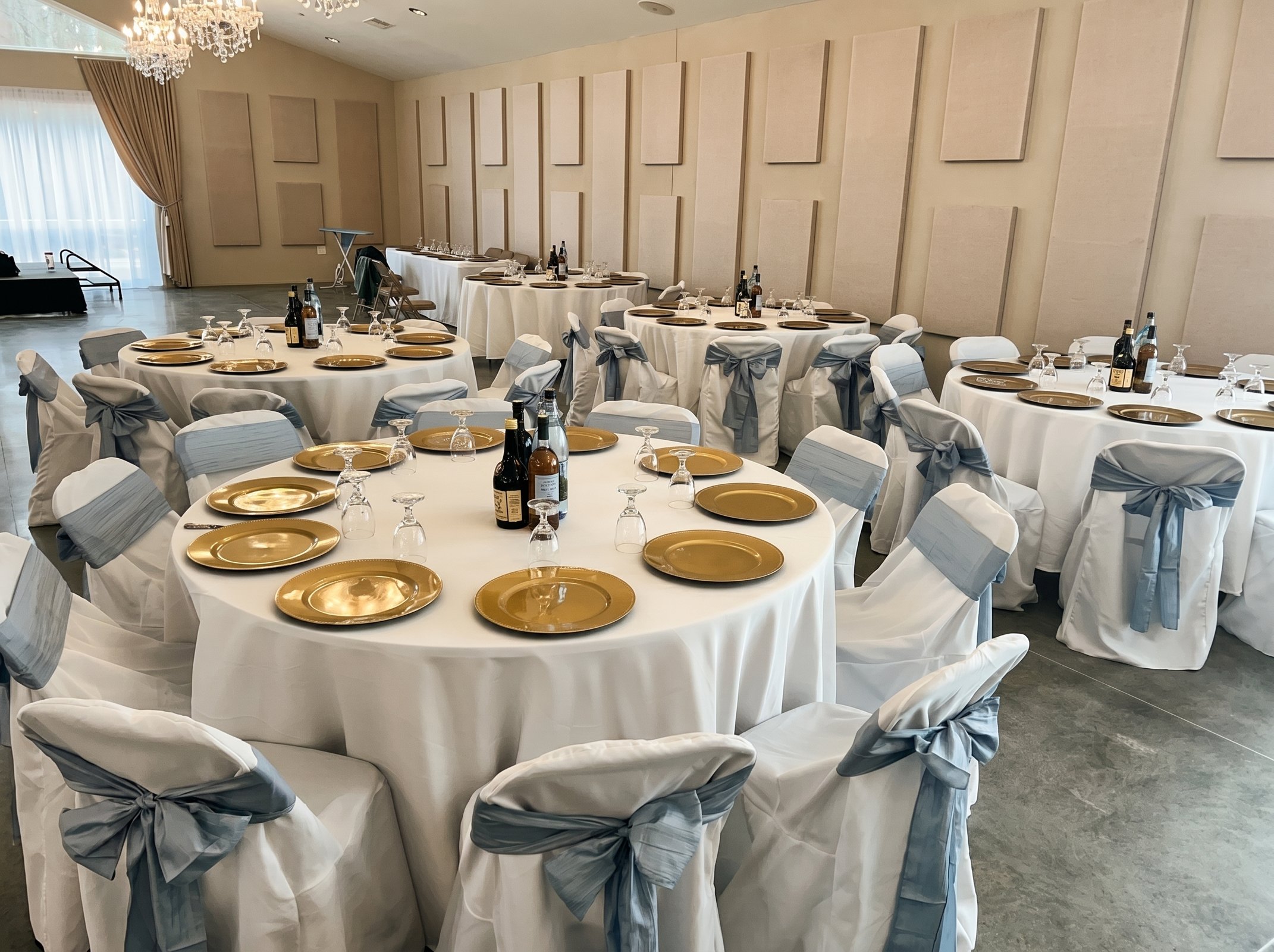 Round reception table set with gold charger plates, stemware and dusty blue chair sashes