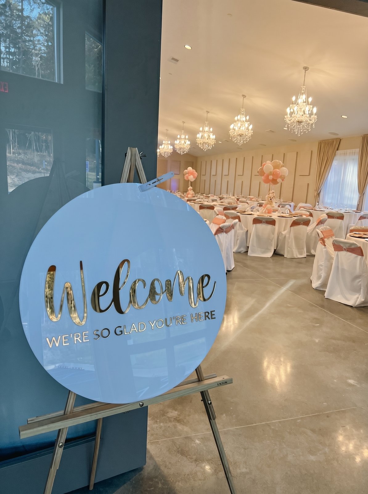 Round welcome sign on an easel at the entrance to a decorated reception in the hall