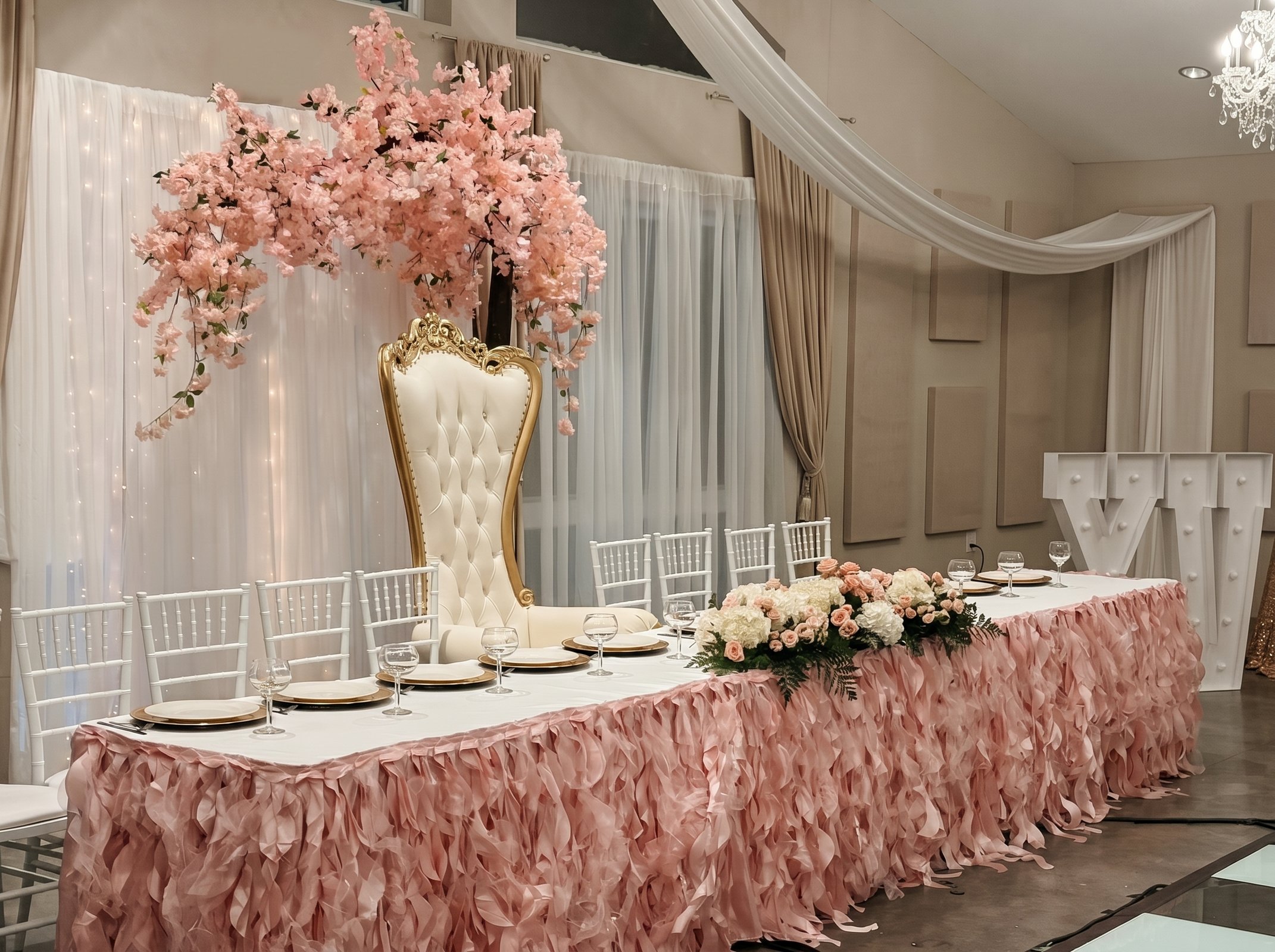 Quinceañera head table with blush ruffled skirting, a tufted throne chair and a cherry blossom centerpiece