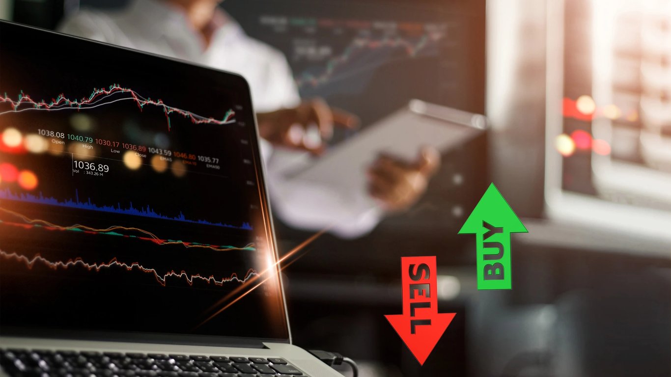 Un trader operando en una laptop con flechas que indican 'buy' y 'sell', representando transacciones de compra y venta