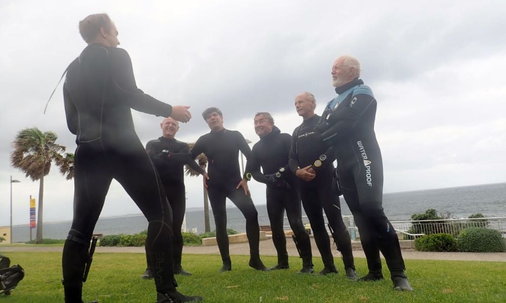 Professional divers in the Divemaster Course briefing, preparing for a dive with their gear in a scenic ocean location.