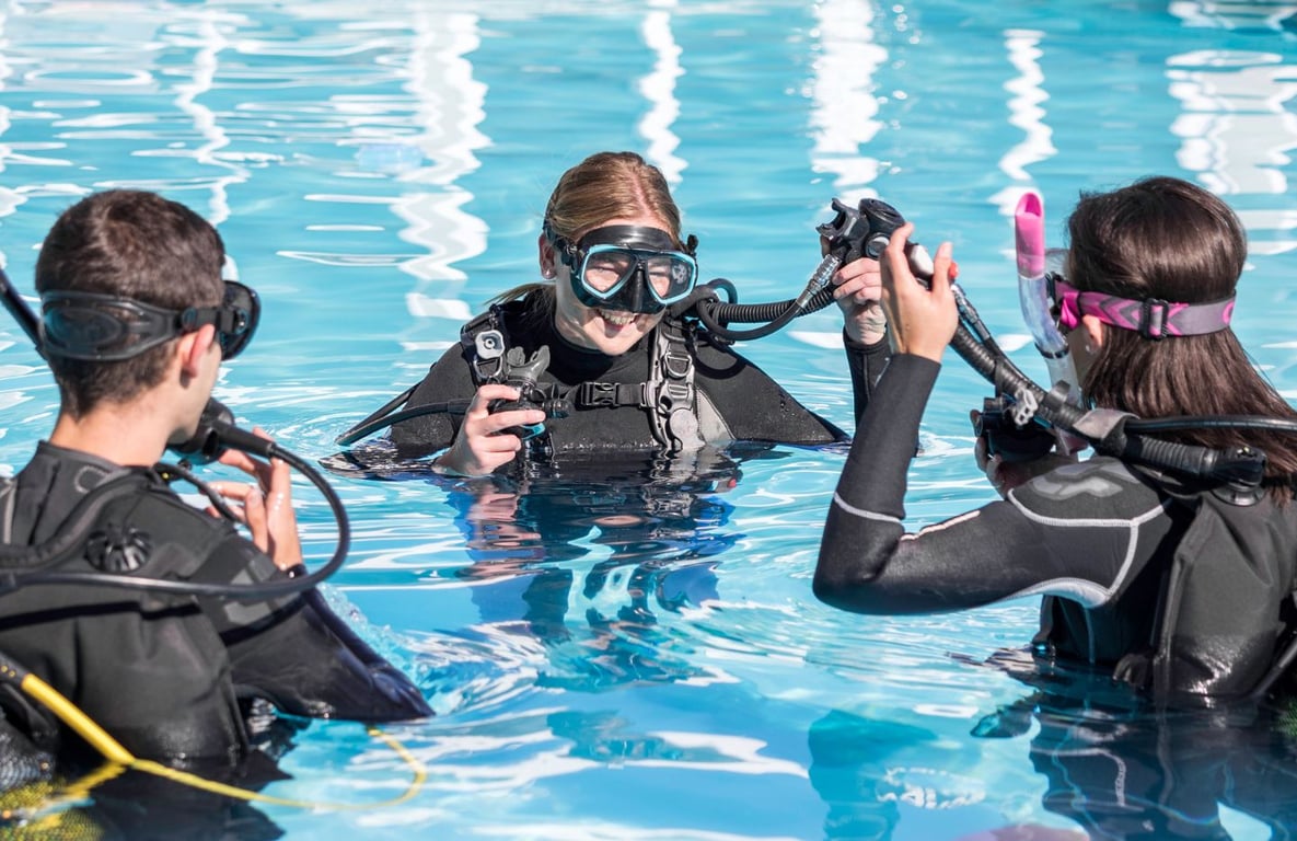 An instructor is demonstrating scuba equipment to a small group of students during a pool training session, emphasizing essential diving skills for their upcoming PADI open water course. The atmosphere is focused and engaging, as participants learn about the gear necessary for their scuba diving adventures.