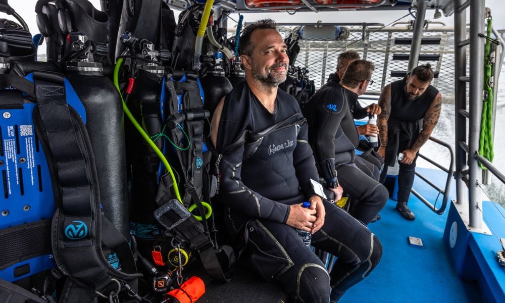 A group of experienced divers in wetsuits is seen preparing their scuba gear on the deck of a boat, ready for an underwater adventure at one of Sydney's iconic dive sites. The atmosphere is filled with excitement as they check their dive equipment, anticipating the diverse marine life they may encounter, including weedy sea dragons and port jackson sharks.