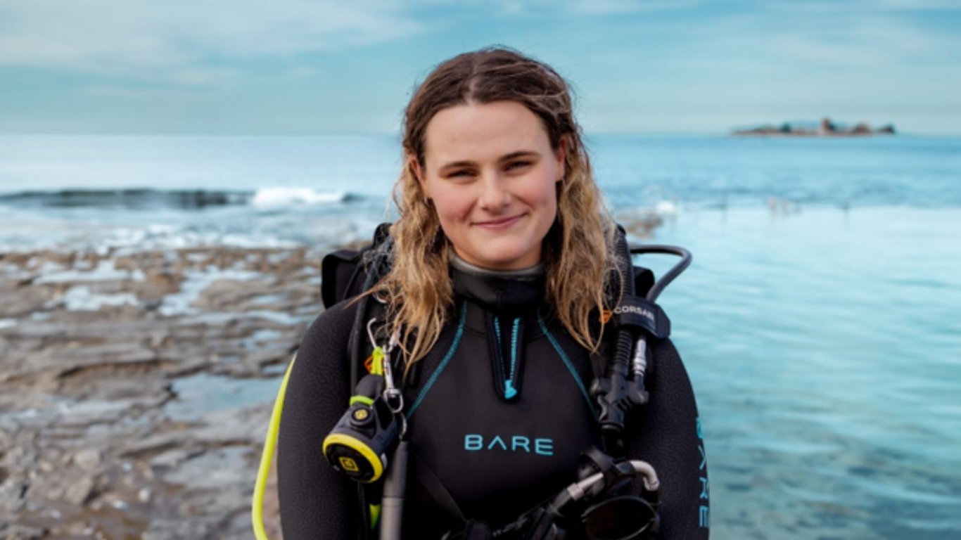 A scuba diver is entering the water from a rocky coastline, equipped with dive gear, ready for an exciting shore dive. The scene captures the anticipation of exploring local dive sites, where diverse marine life awaits beneath the surface.