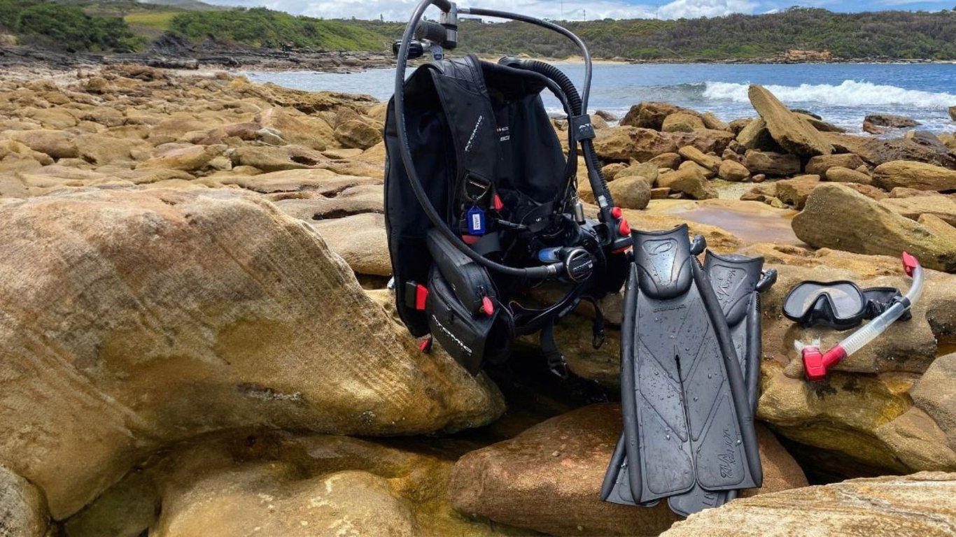 Professional scuba diving equipment is neatly arranged on a shore line, showcasing essential items such as a BCD, regulator, wetsuit, and fins, ready for a scuba diving adventure in Australia. This setup reflects the quality and safety focus of dive courses, ensuring certified divers are equipped for exploring the amazing marine life of the Great Barrier Reef.