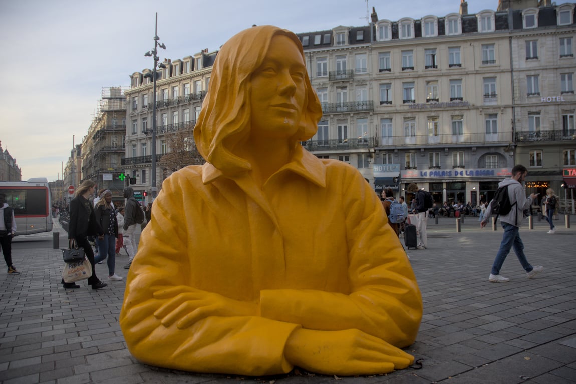 A bright yellow bust of a woman with arms folded