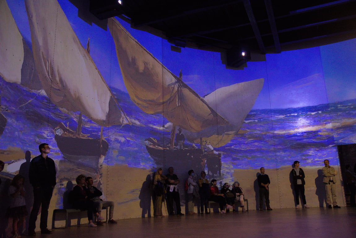 A painting of sailboats on a sandy beach, projected onto the walls