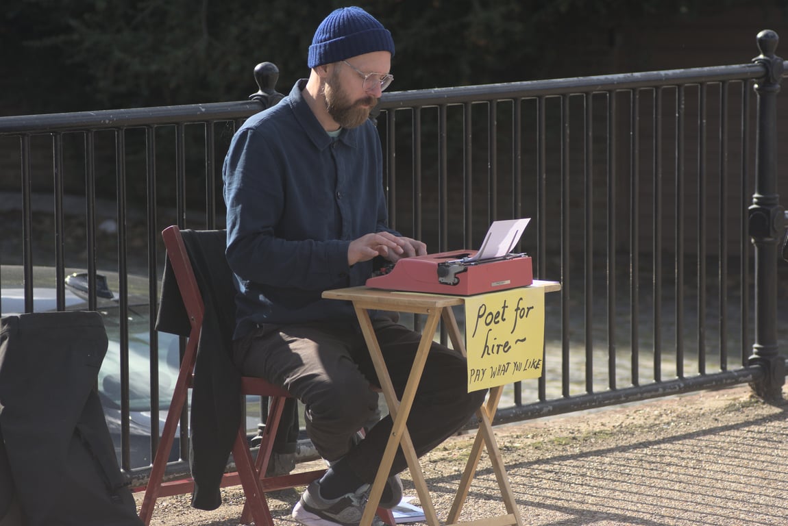 Man sitting at a typewriter.
        Sign: Poet for hire, Pay what you like.