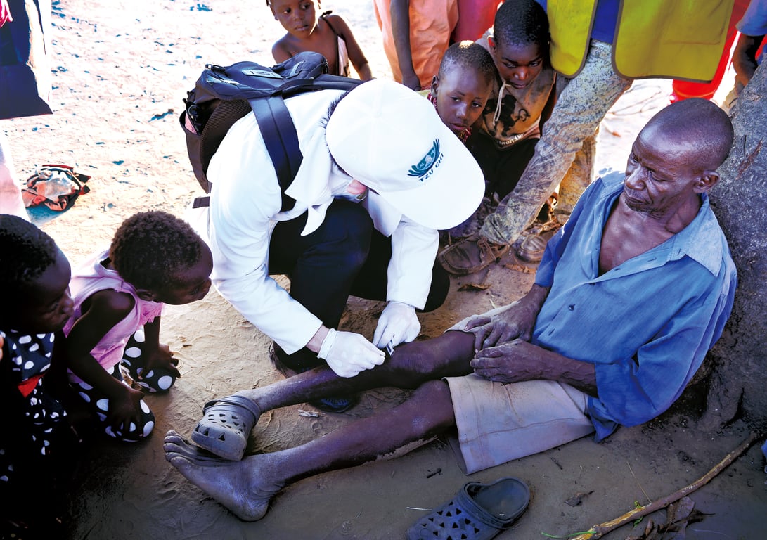 慈濟醫護前往莫三比克往診、訪視；一位老先生拿著樹枝當拐杖，一跛一跛的走來。醫師立刻讓他就地靠在樹幹休息，並蹲下為他治療。看診時，許多孩童圍在旁邊，如同一幅佛陀問病圖。