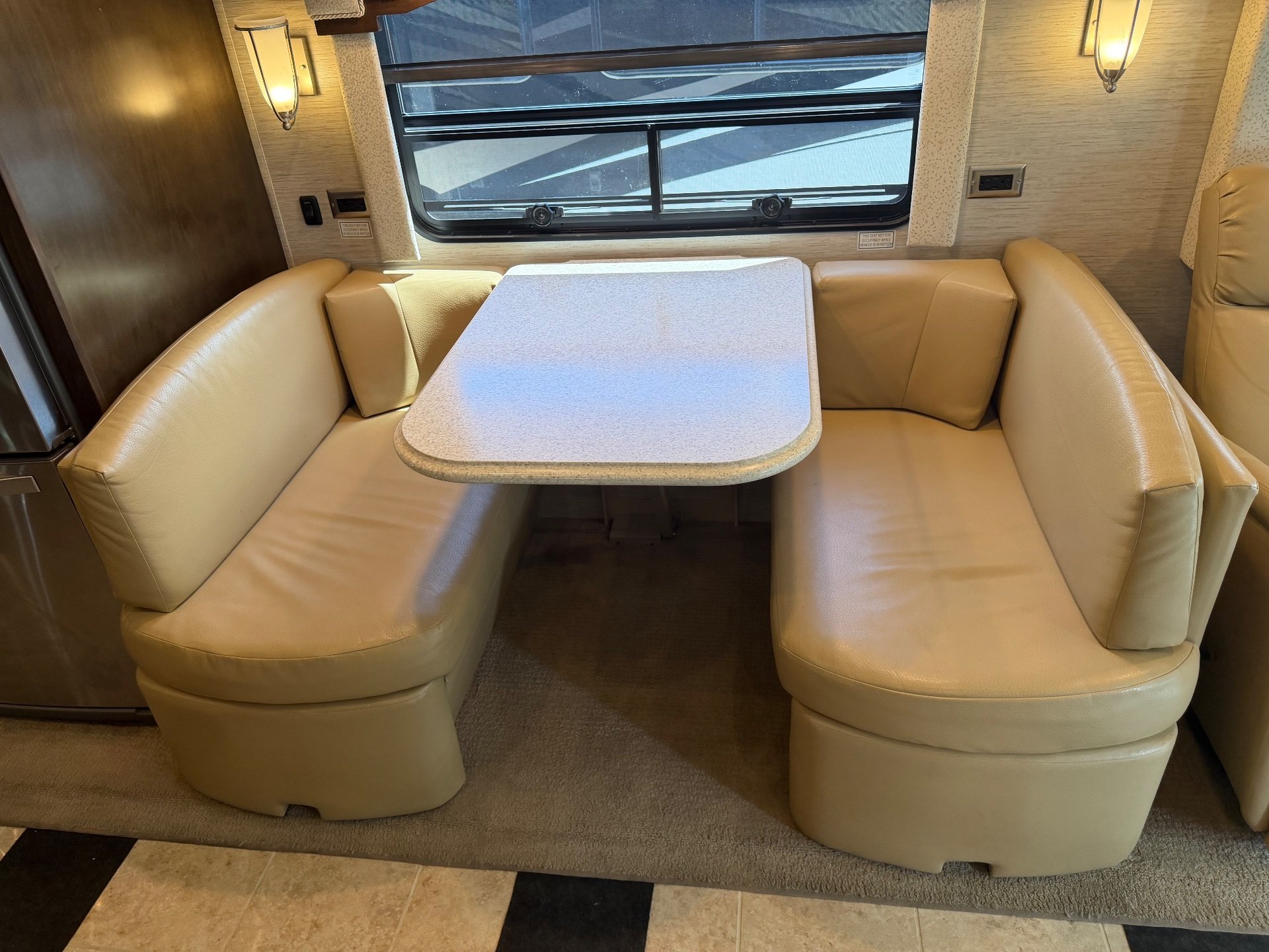 2018 Newmar Ventana 4369 — U-shaped dinette with tan booth seating, tabletop, window, and surrounding wall lighting