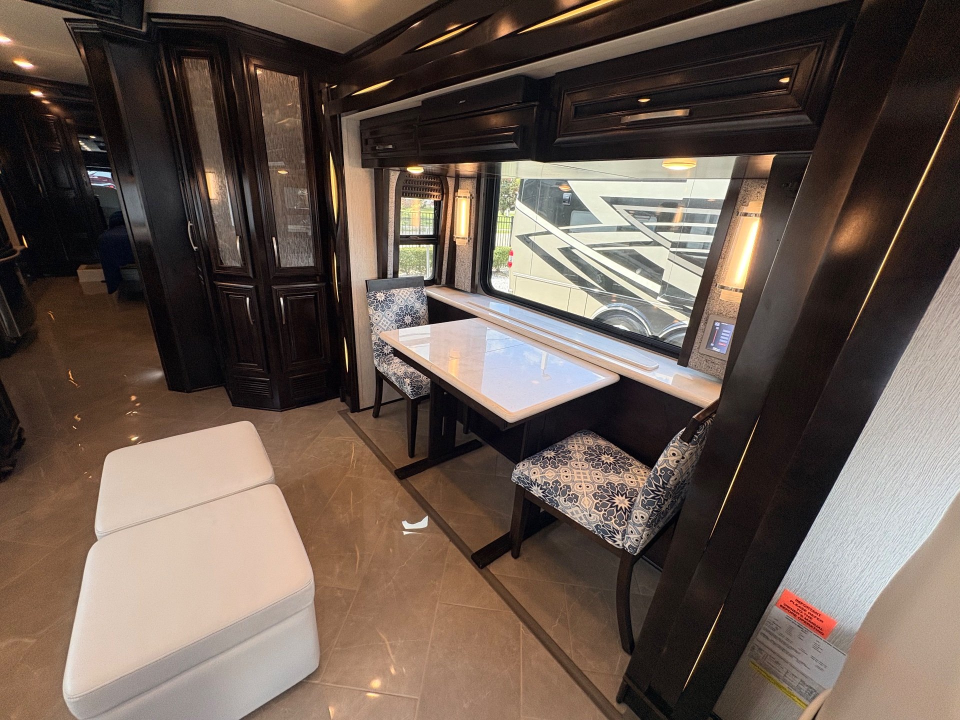 2021 Newmar New Aire 3545 — Dining table and upholstered chairs beside a lounge ottoman, with cabinetry and hallway visible