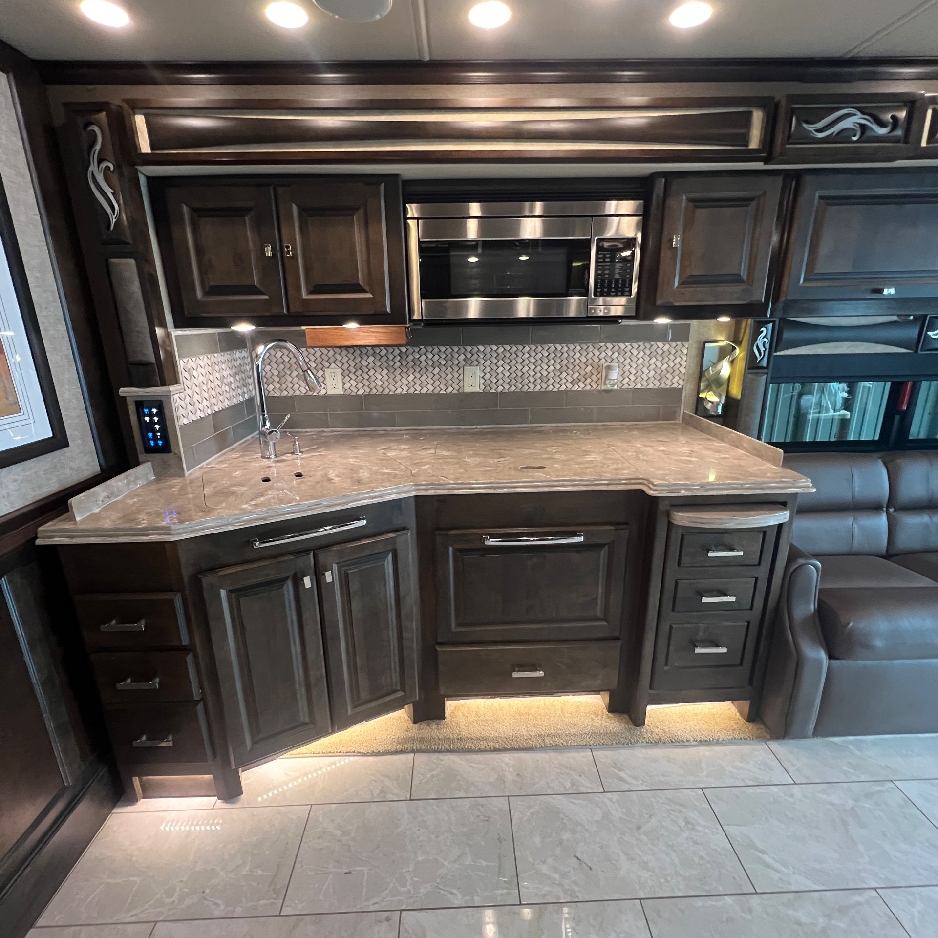 2018 Tiffin Phaeton 40 IH — Motorhome kitchen with sink, broad countertop, microwave, backsplash, cabinetry, and sofa at right