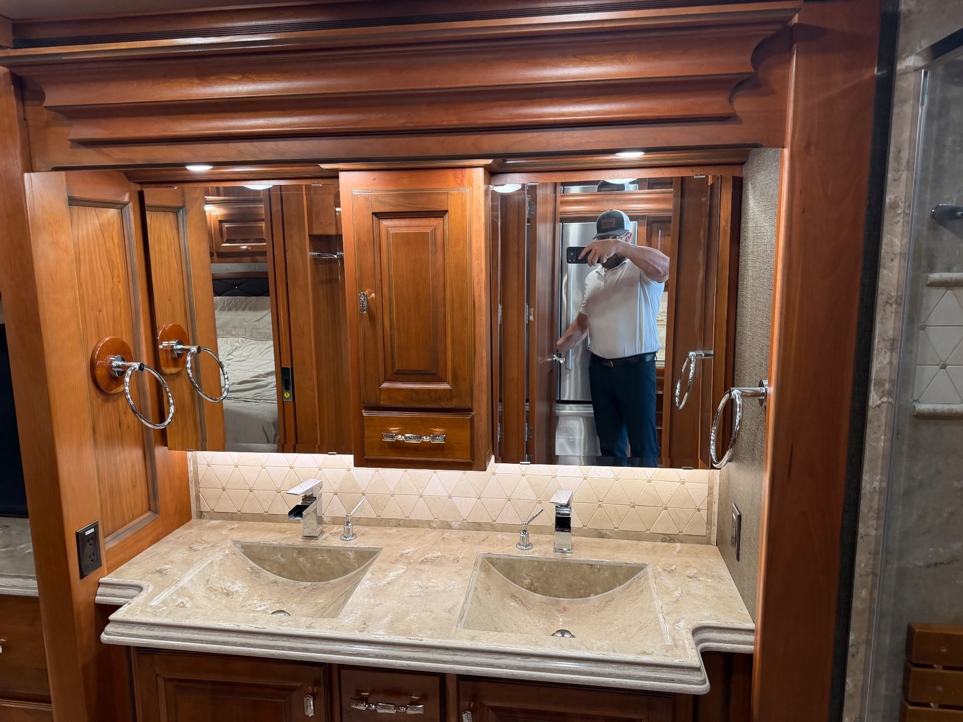 2017 Tiffin Allegro Bus 37 AP — Bathroom vanity with double sinks, mirrored medicine cabinets, wood cabinetry, and a partial glass shower enclosure