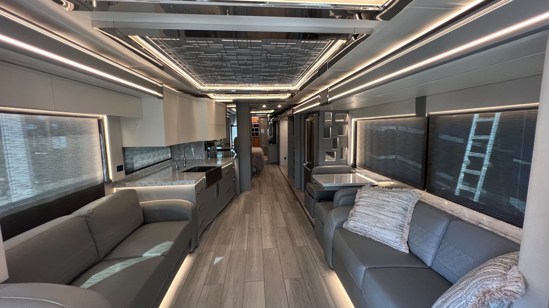 2025 Newmar King Aire 4558 — Class A motorhome interior with opposing sofas, kitchen cabinetry, dining seating, and a long central aisle