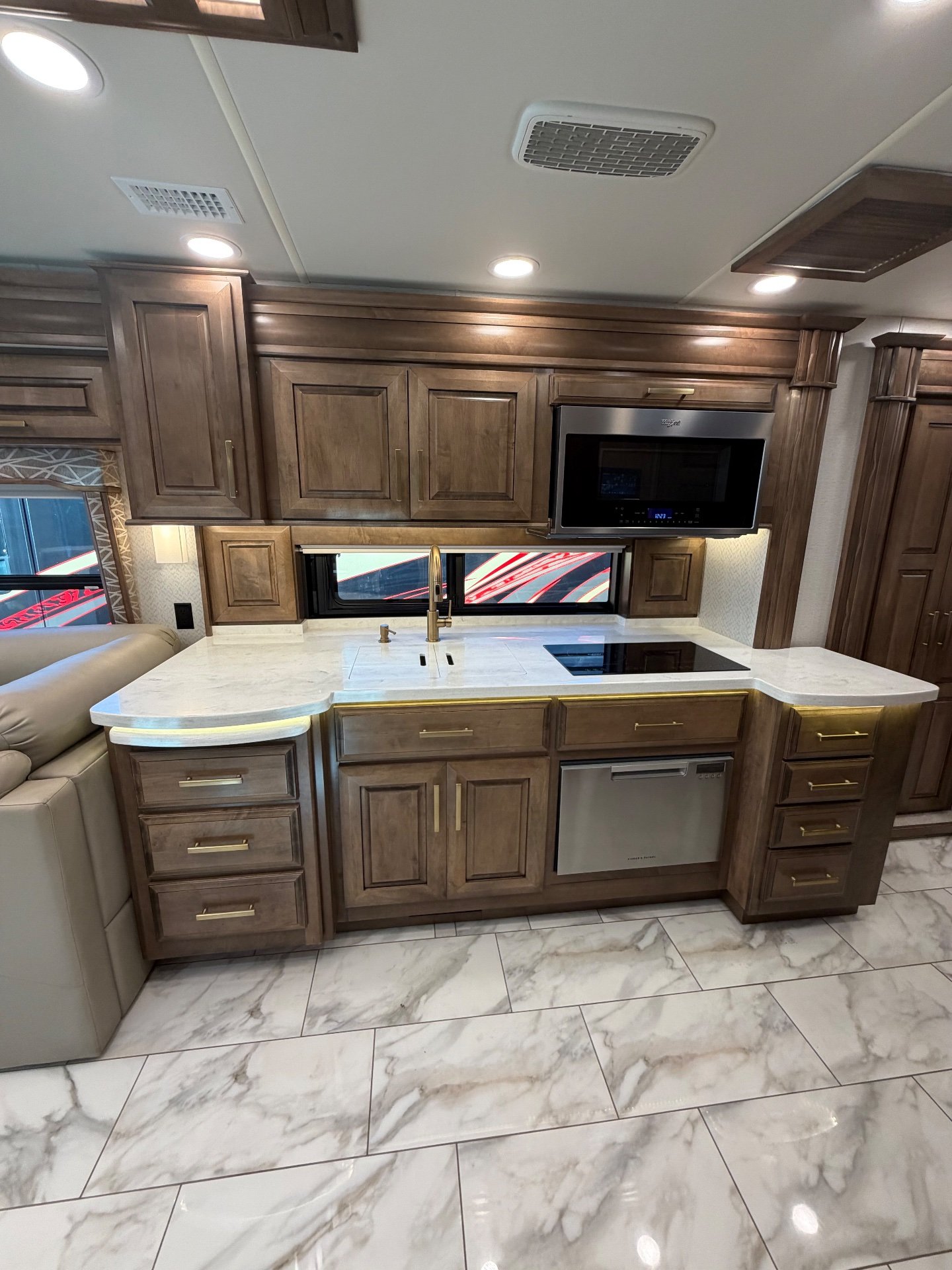 2022 Entegra Coach Cornerstone 45B — Motorhome kitchen with sink, induction cooktop, microwave, dishwasher, counters, and adjacent sectional edge