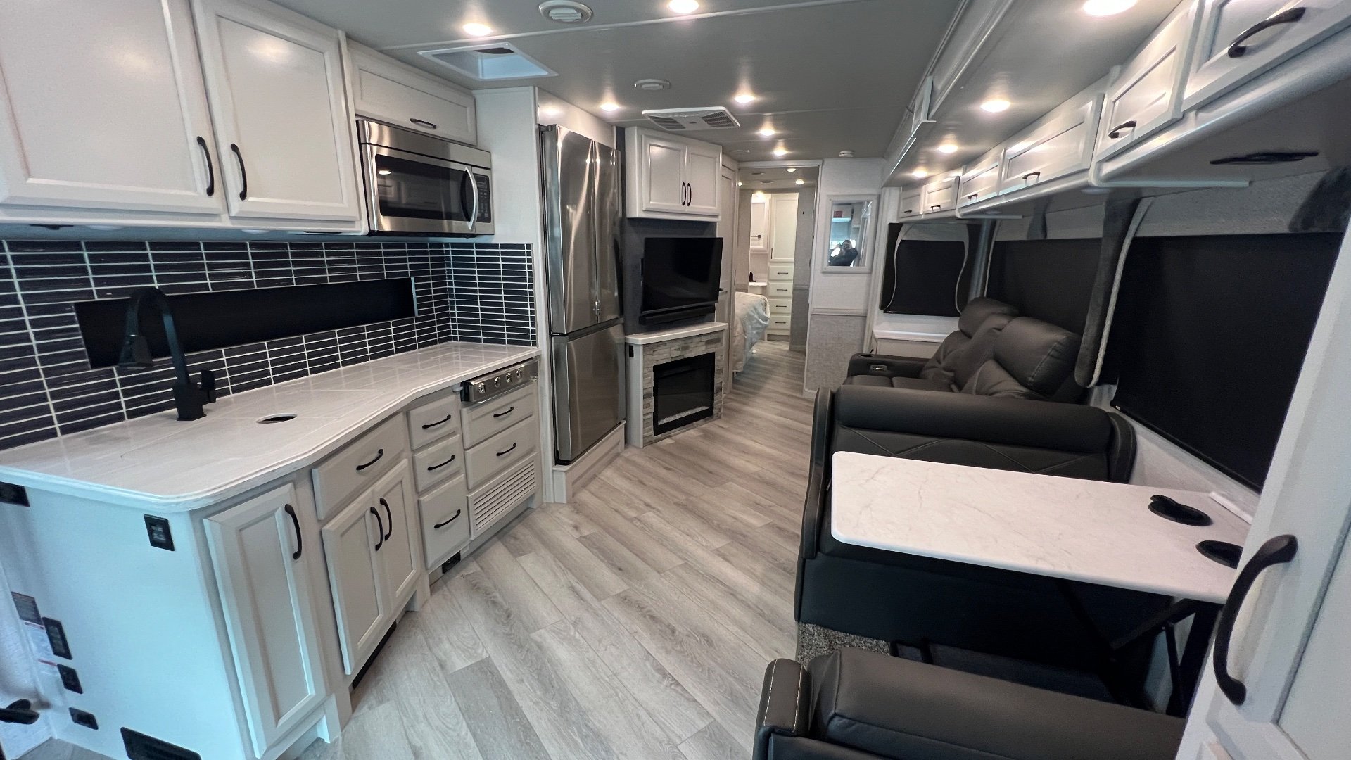 2024 Fleetwood Bounder 35K — Class A motorhome interior showing kitchen appliances and backsplash beside lounge seating, dinette, and central entertainment wall