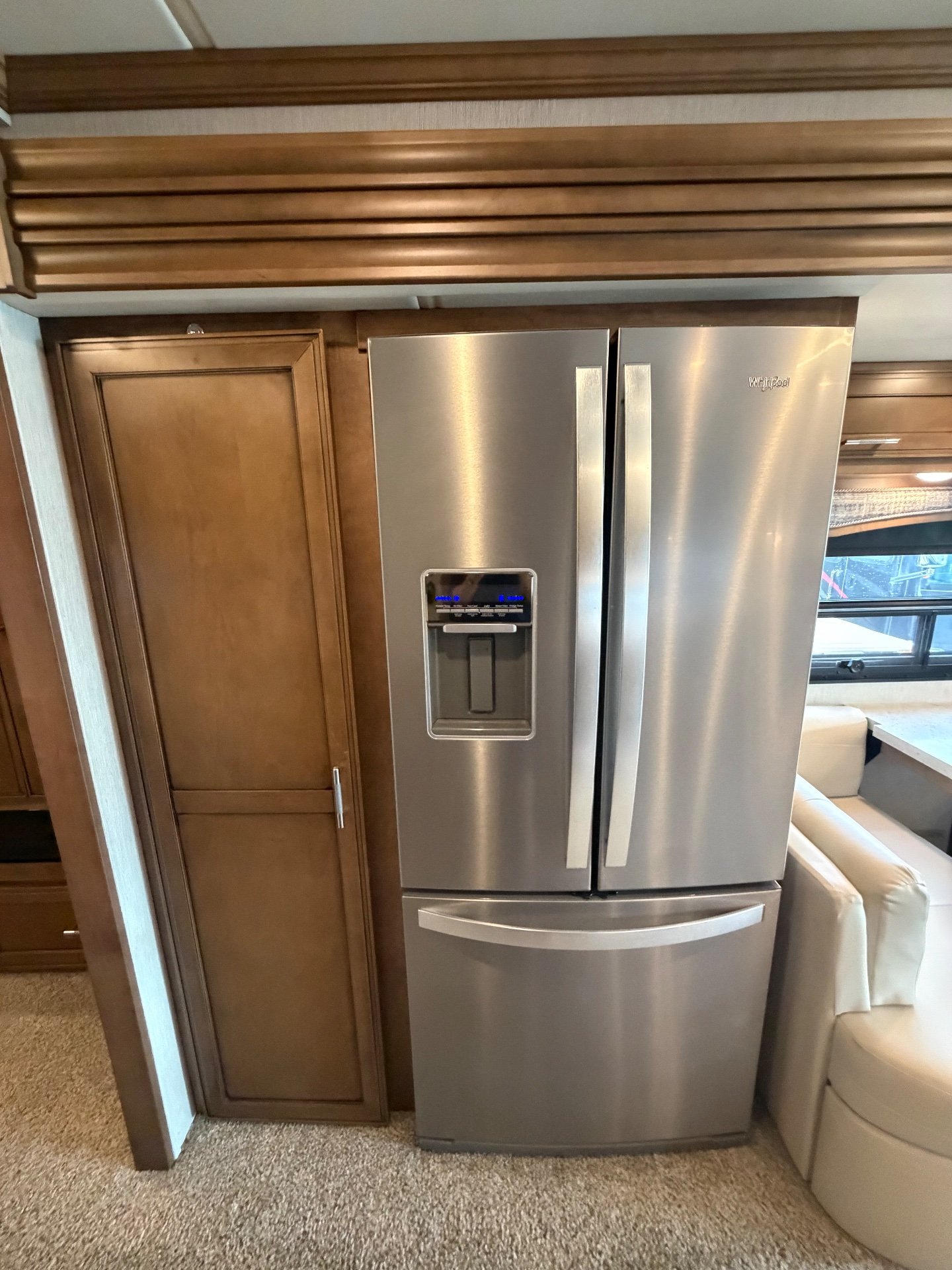 2020 Newmar Ventana 4369 — Stainless French-door refrigerator with water dispenser beside a tall wood-paneled cabinet