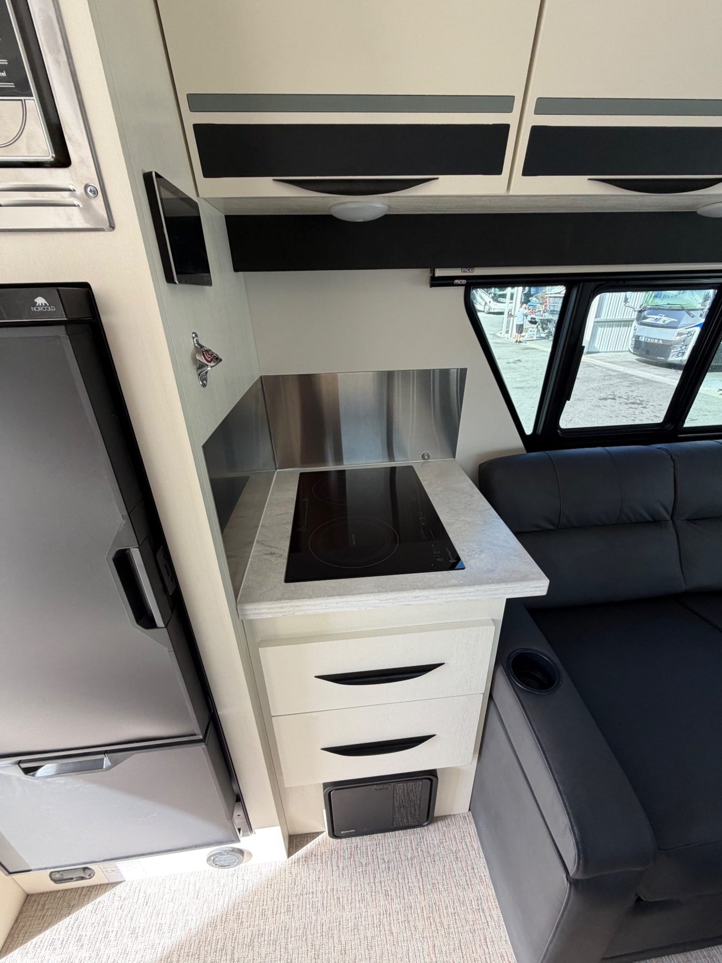 2026 Chinook RV Summit DS — Compact kitchen with induction cooktop, stainless backsplash, drawers, and adjacent refrigerator