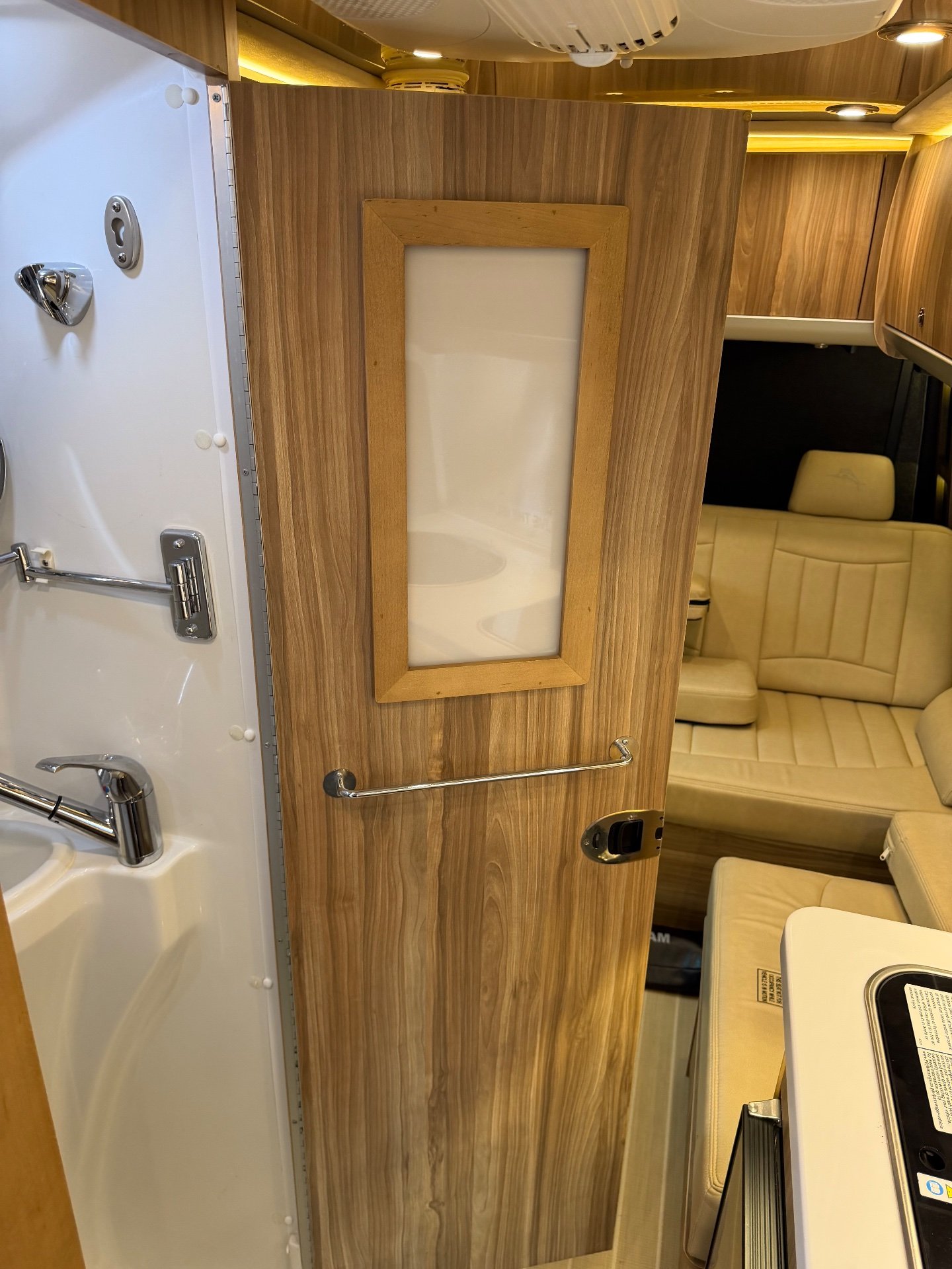 2020 Airstream Interstate 24GL 4WD — Open bathroom door with sink and mirror panel beside the van lounge seating and kitchen counter