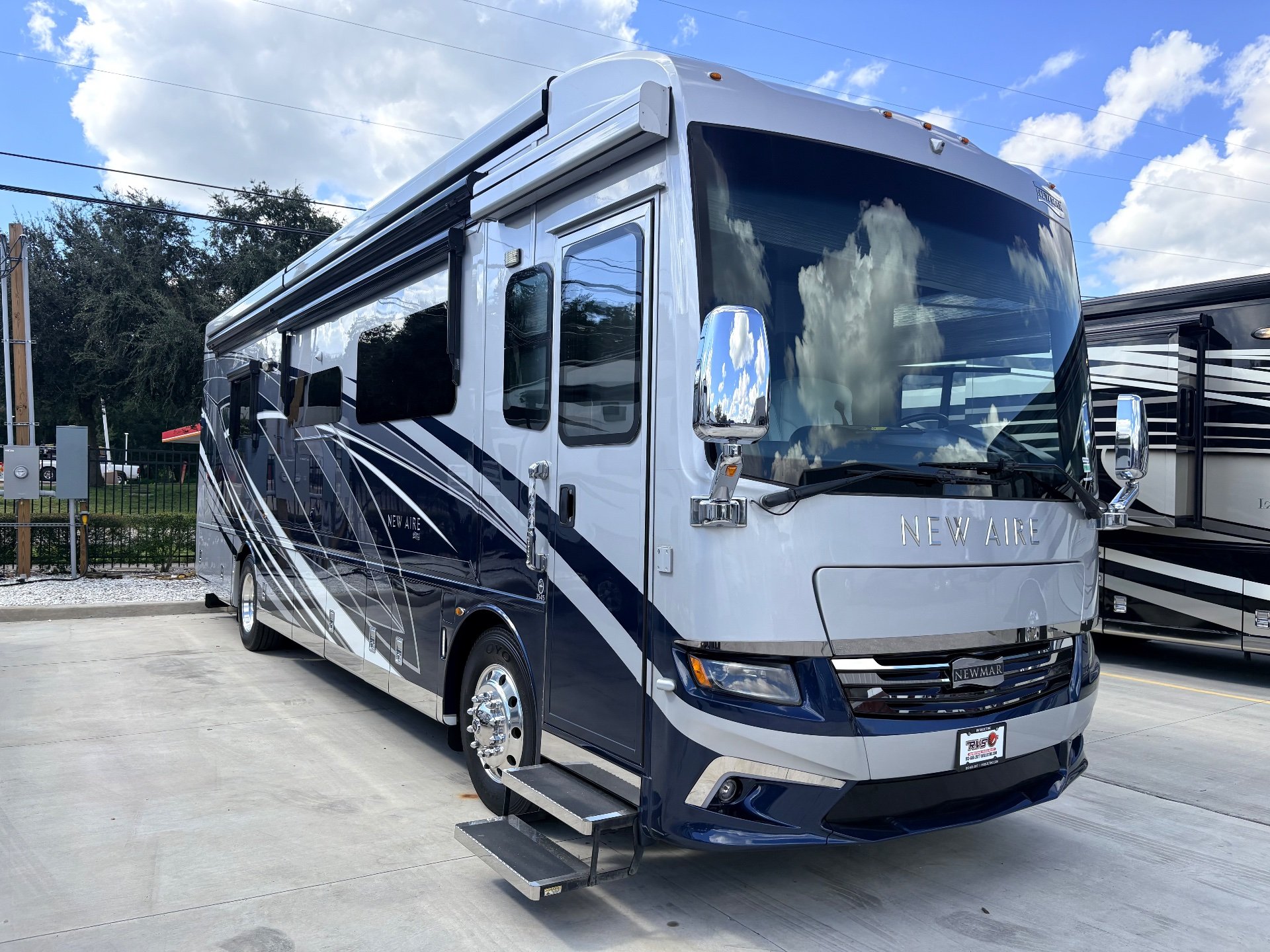 2021 Newmar New Aire 3545 — Front-side exterior photograph shows the RV shell, entry door, deployed steps, windshield, and side awnings