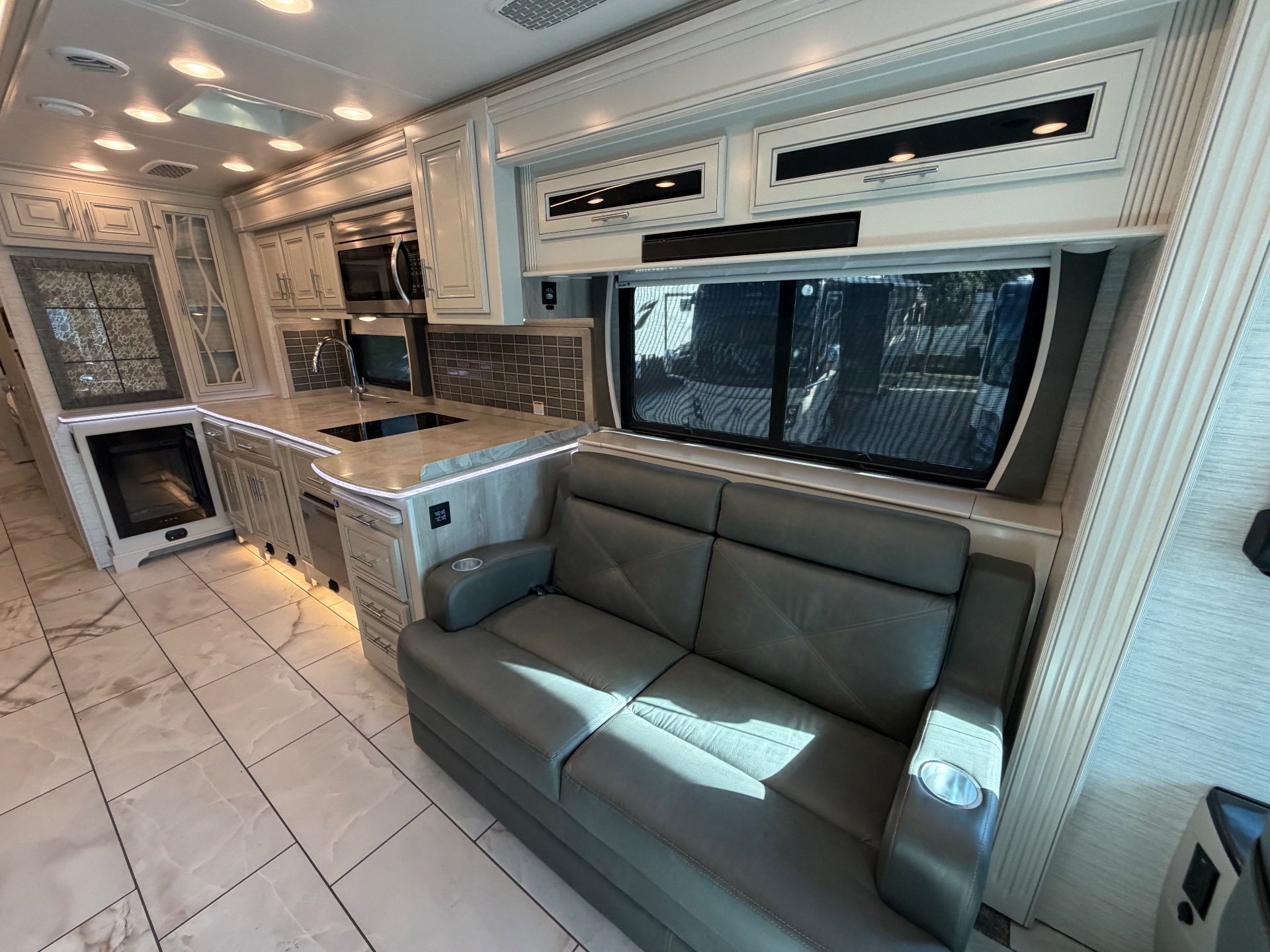 2023 Forest River Berkshire XLT 45E — Motorhome kitchen with island, sink, cooktop, microwave, backsplash, and adjacent sofa beneath a window