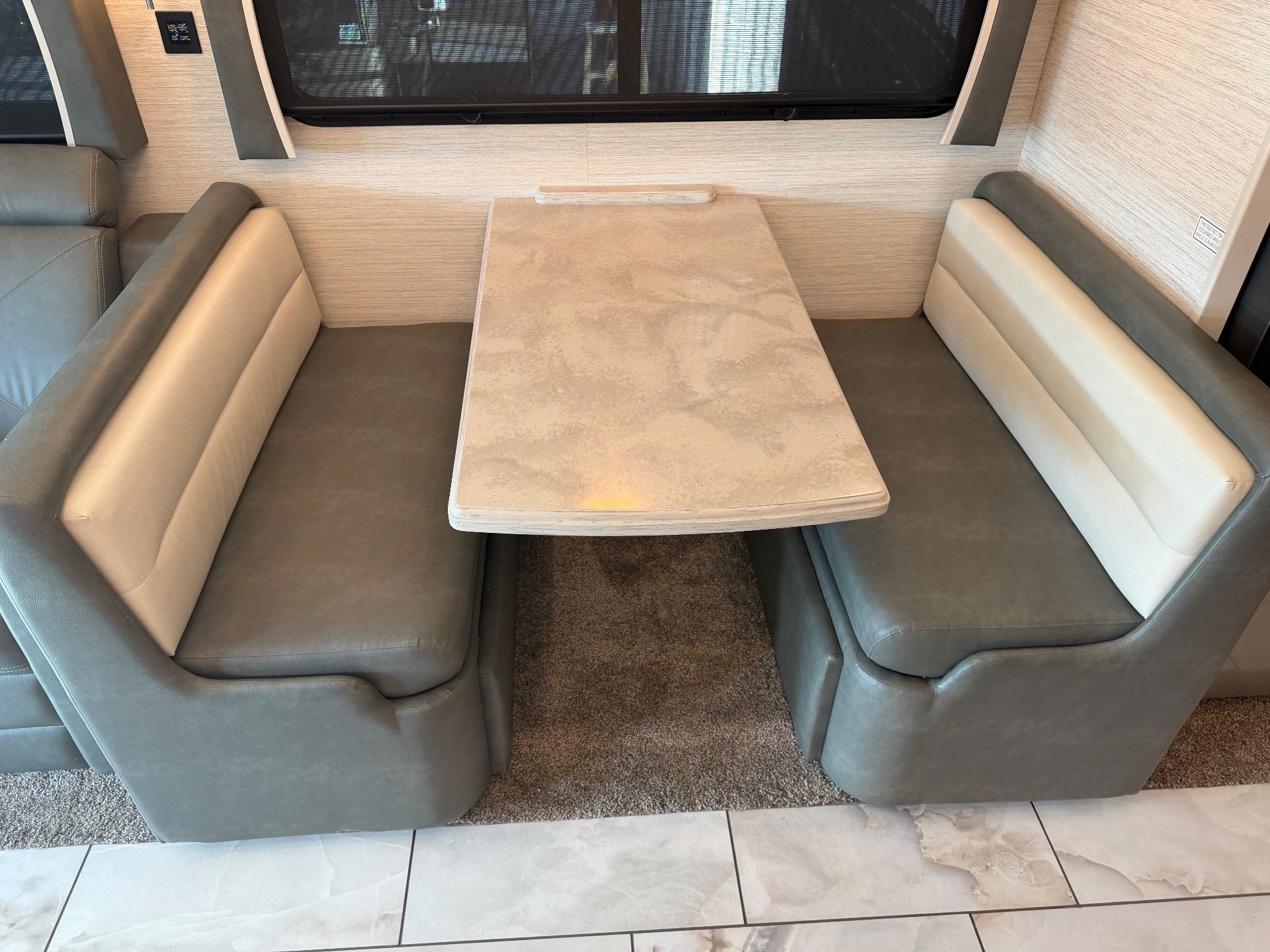 2023 Forest River Berkshire XLT 45E — Freestanding dining table surrounded by two opposing upholstered bench seats beneath a window