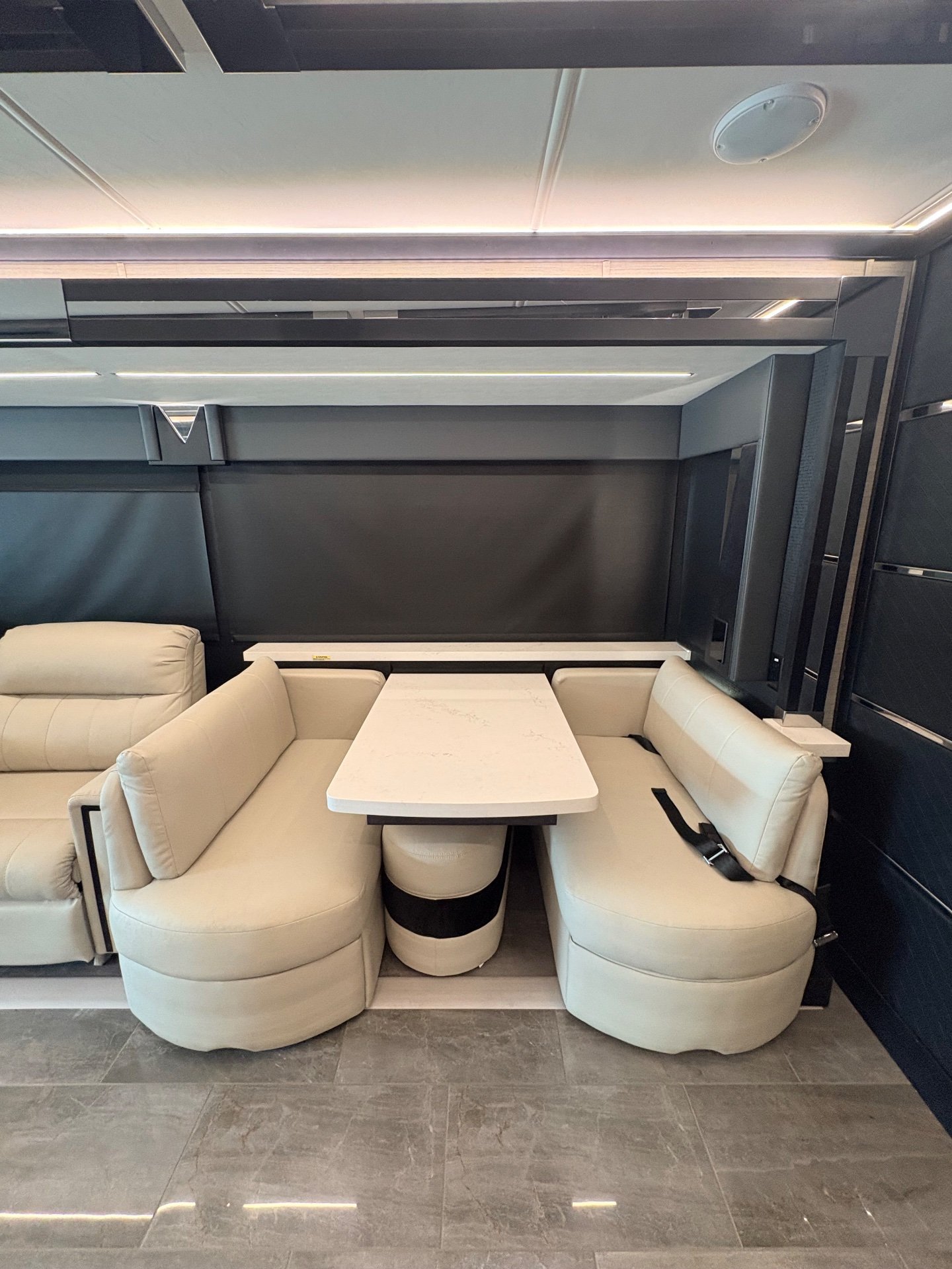 2025 Tiffin Zephyr 45 PZ — Dining booth with a rectangular table and two facing benches beside adjacent living-room seating
