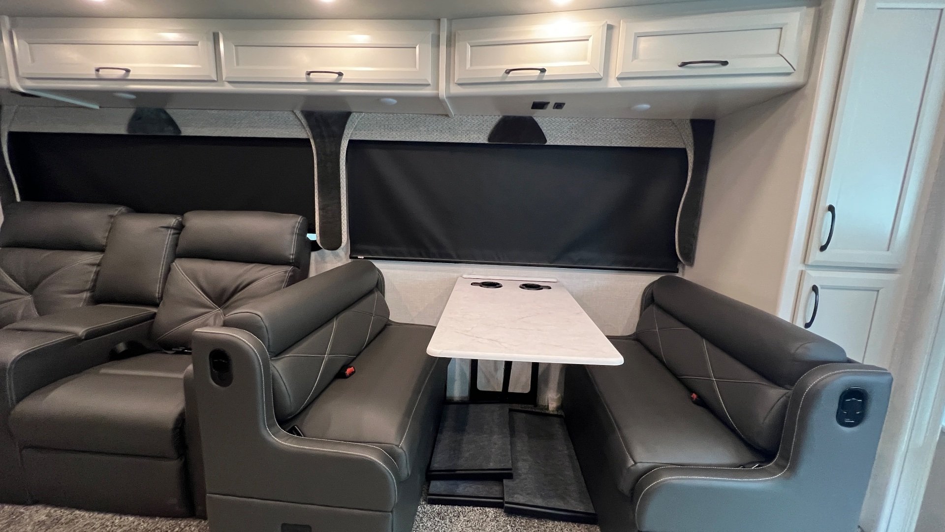 2024 Fleetwood Bounder 35K — Motorhome dinette with opposing upholstered benches, table, overhead cabinets, and covered windows