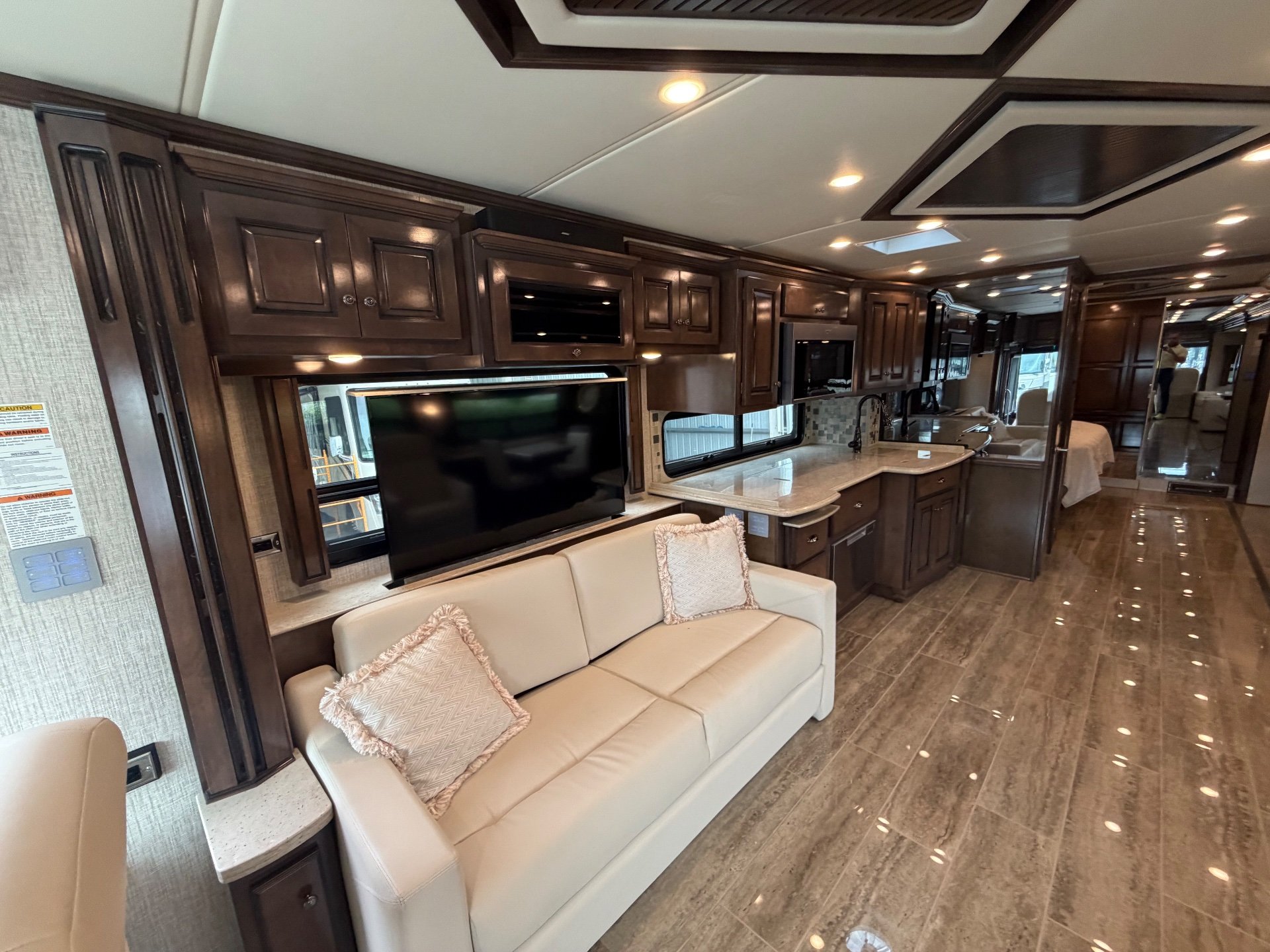 2021 Newmar Dutch Star 4369 — Motorhome sofa beneath a television facing a kitchen peninsula with sink, counters, appliances, and overhead cabinets