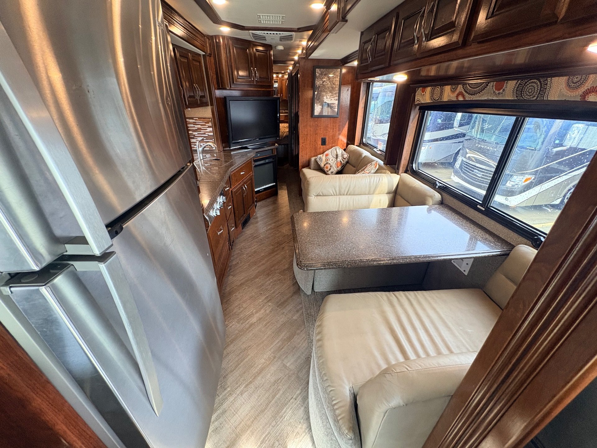 2019 Fleetwood Pace Arrow LXE 38N — Motorhome interior overview centered on dinette table with sofa, refrigerator, kitchen counter, and television