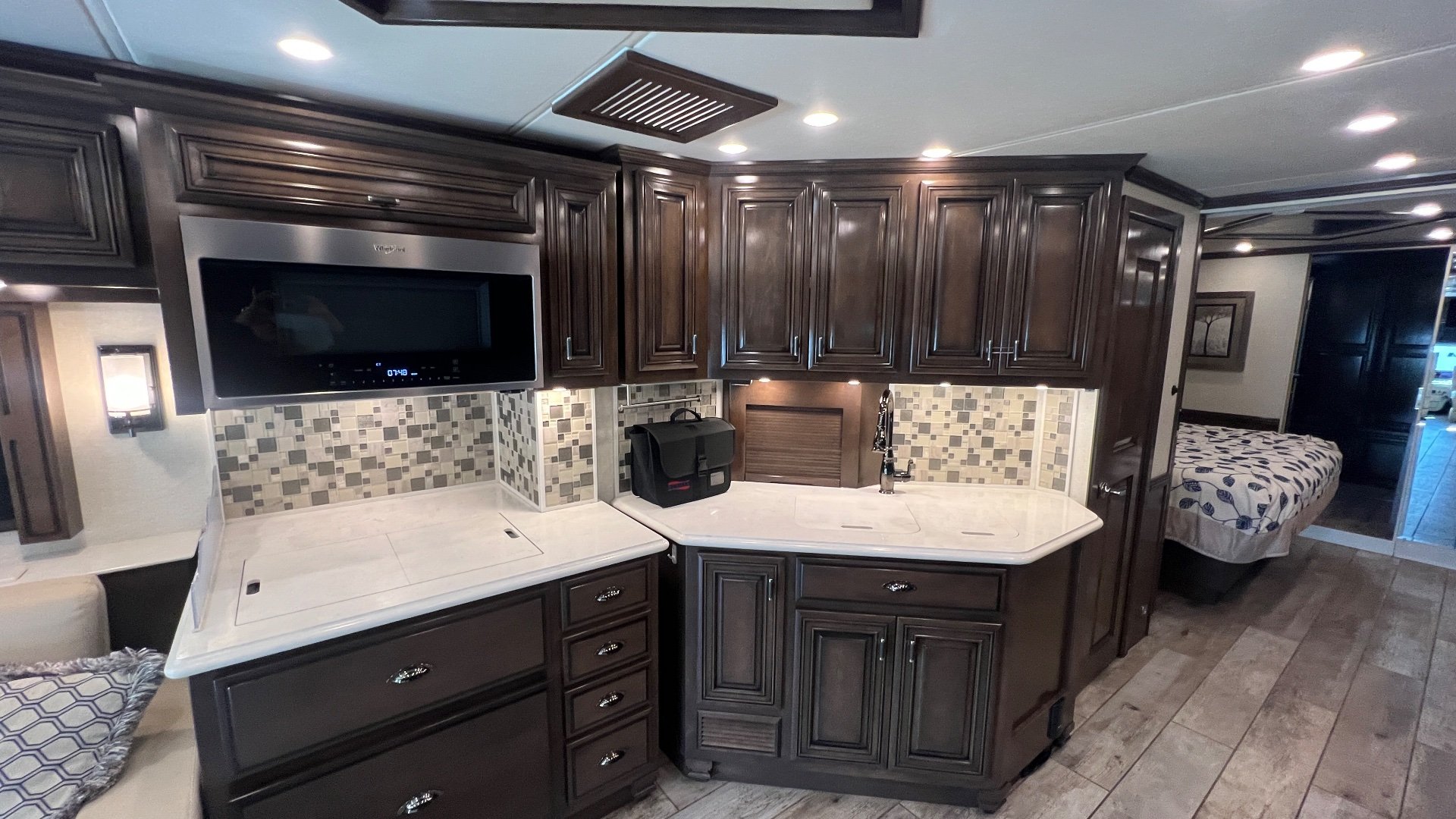 2020 Newmar Dutch Star 4328 — Class A kitchen with microwave, counters, sink, mosaic backsplash, and cabinetry opening toward a visible bed