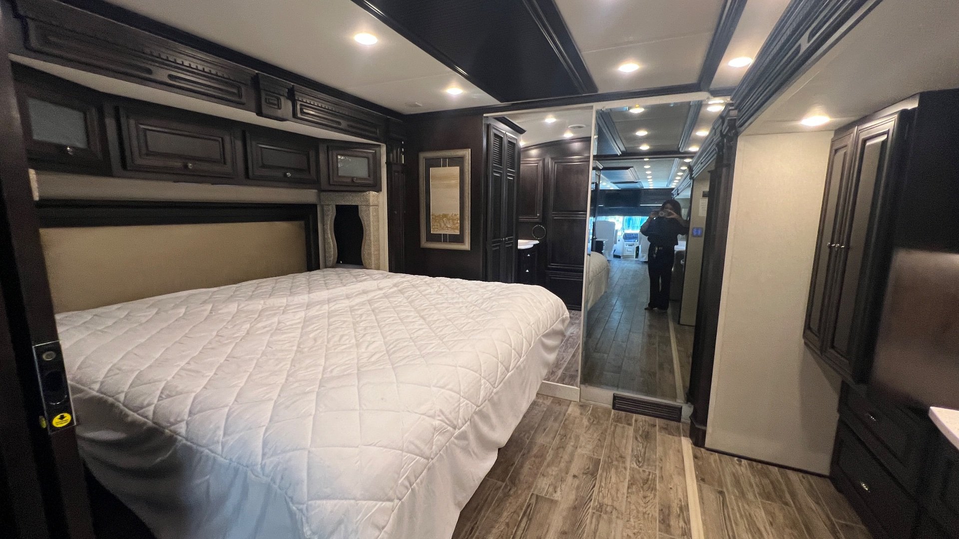 2018 Newmar Dutch Star 4369 — Main bedroom with a large bed, overhead cabinets, side wardrobe, dresser, and hallway extending toward the front