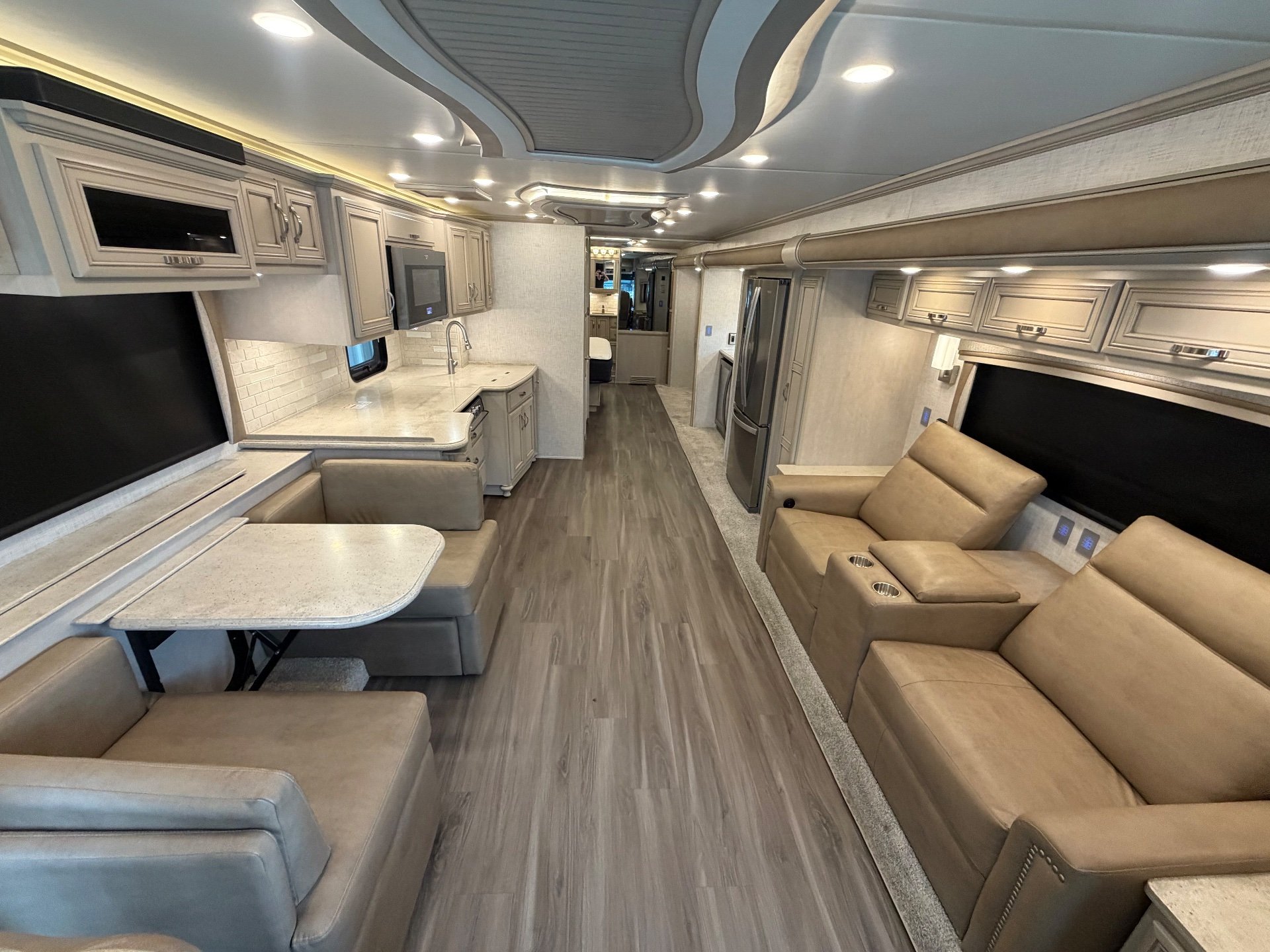 2023 Newmar Kountry Star 4068 — Motorhome interior overview with sofas, recliners, dinette, television, kitchen counters, sink, and refrigerator