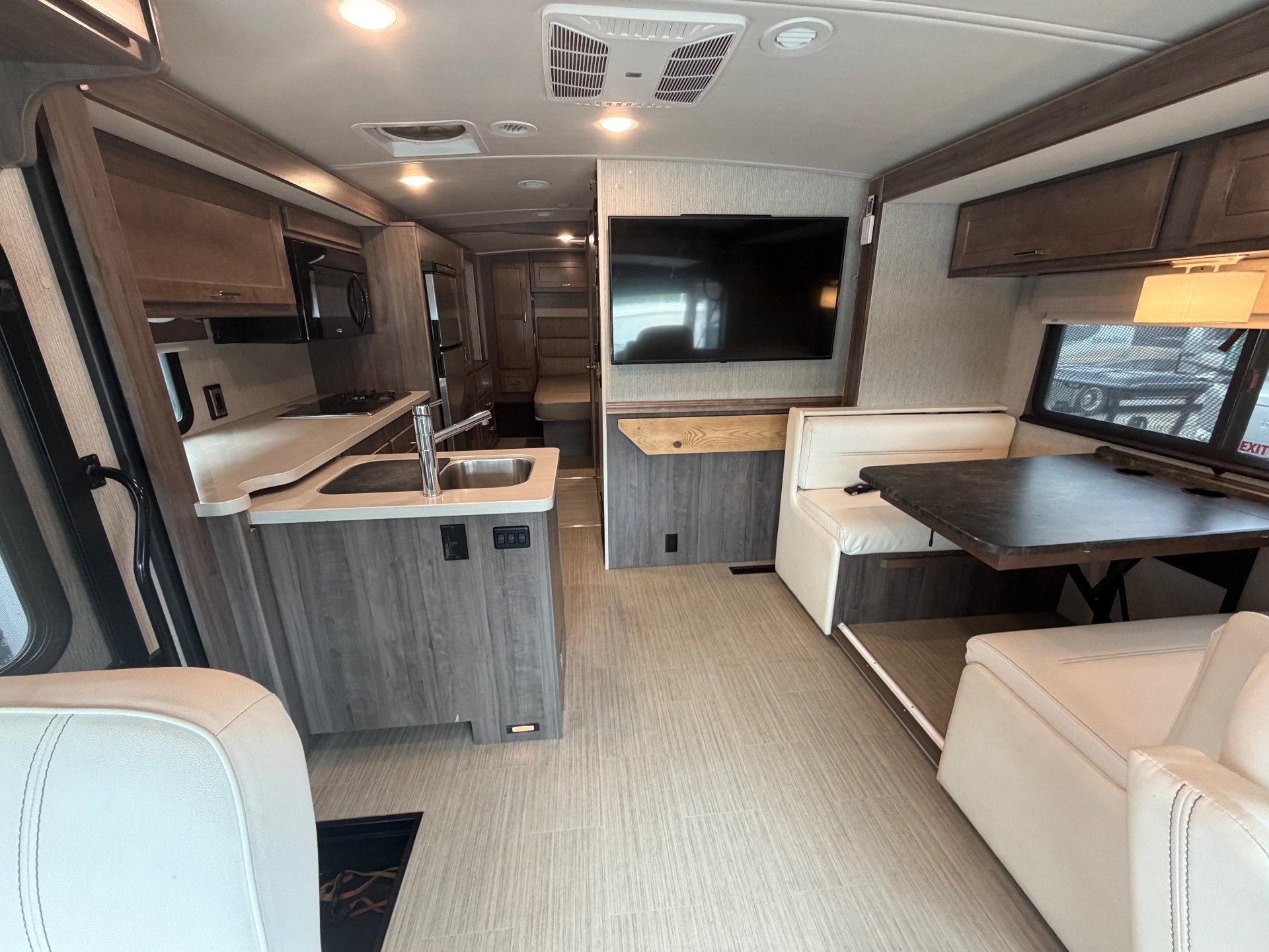2021 Winnebago Adventurer 27N — Class A motorhome interior with lounge seating, dinette, entertainment center, and adjacent kitchen island
