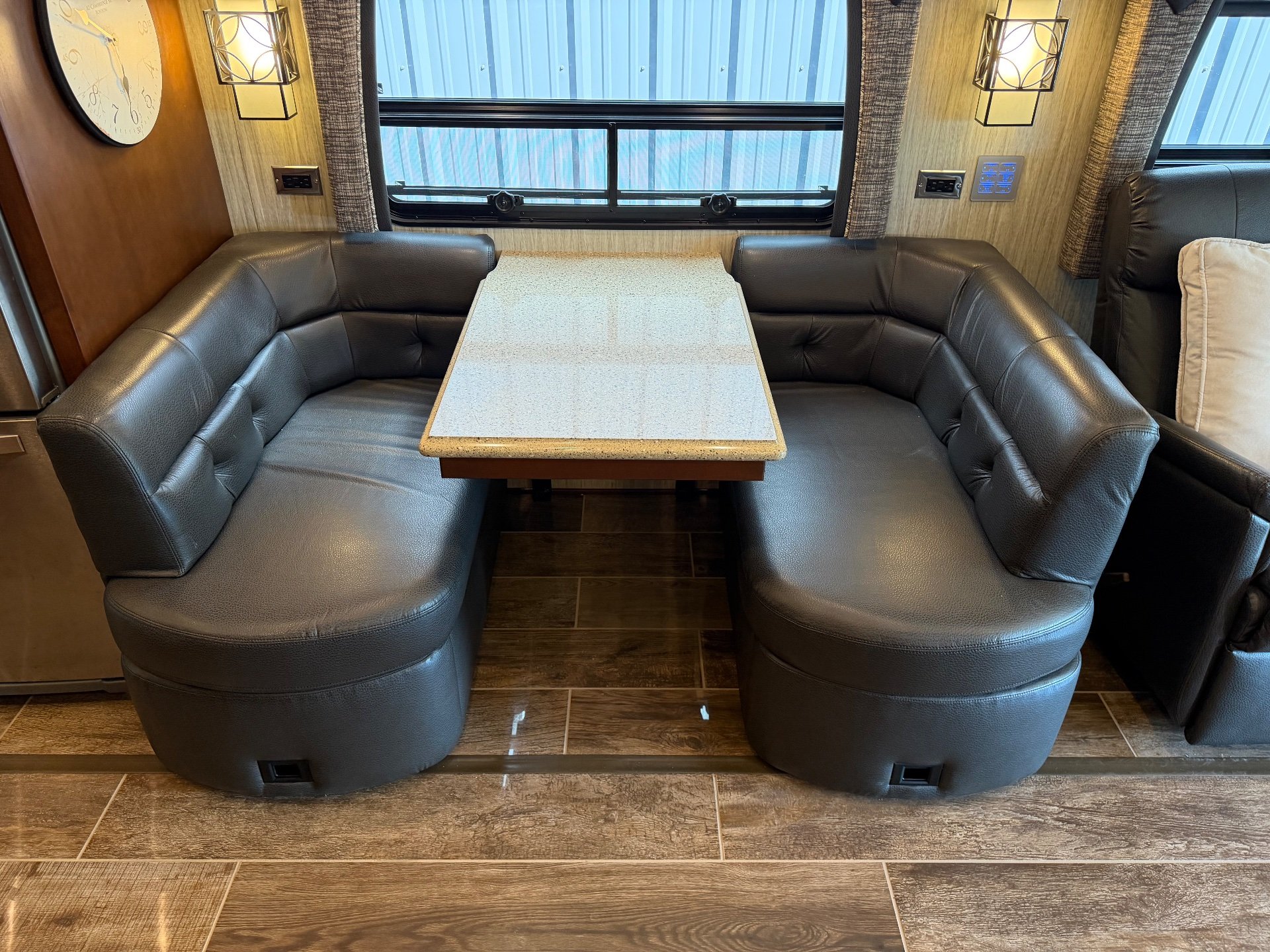 2017 Newmar Dutch Star 4369 — Leather booth dinette surrounds a rectangular tabletop beneath a large window, with wall lighting and controls